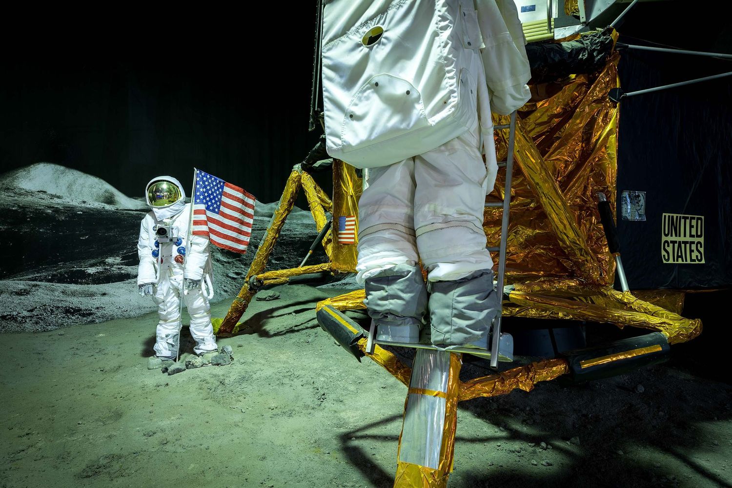 Astronauts in white spacesuits stand on the moon surface near an American flag and a lunar lander module.