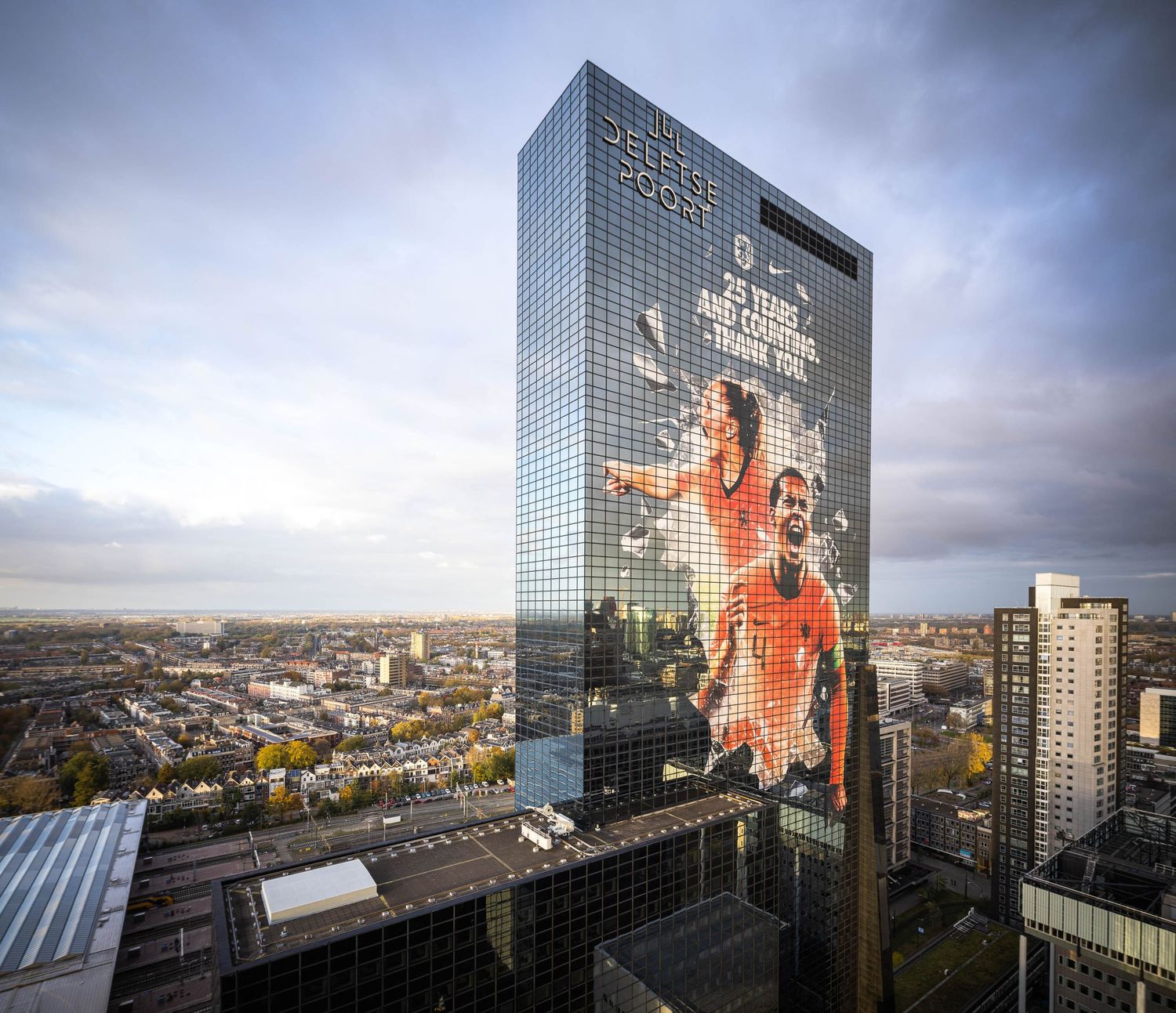 A massive sports advertisement featuring football players displayed on the glass facade of a modern skyscraper in a city skyline.