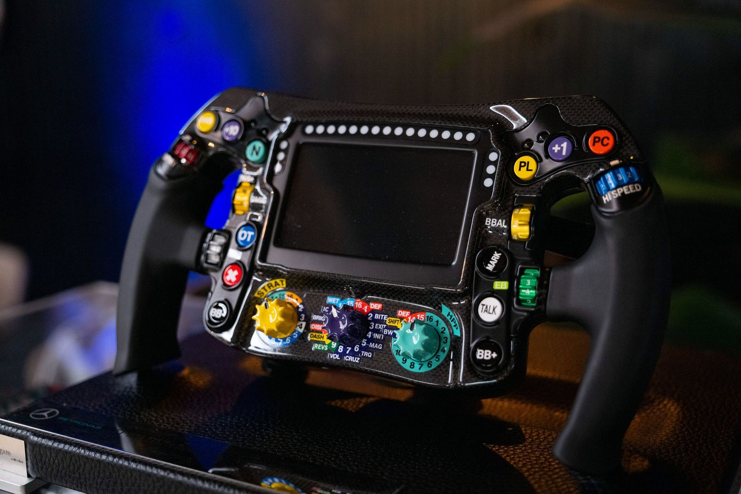 Formula 1 racing steering wheel with colorful buttons and digital display in low light.