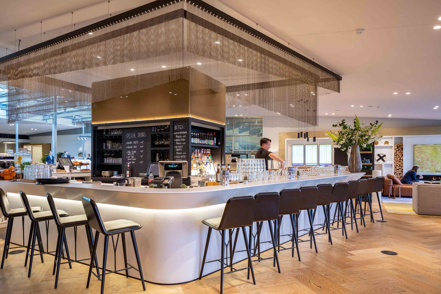 Modern office cafeteria with sleek bar seating, white counters, and minimalist design elements throughout the space.