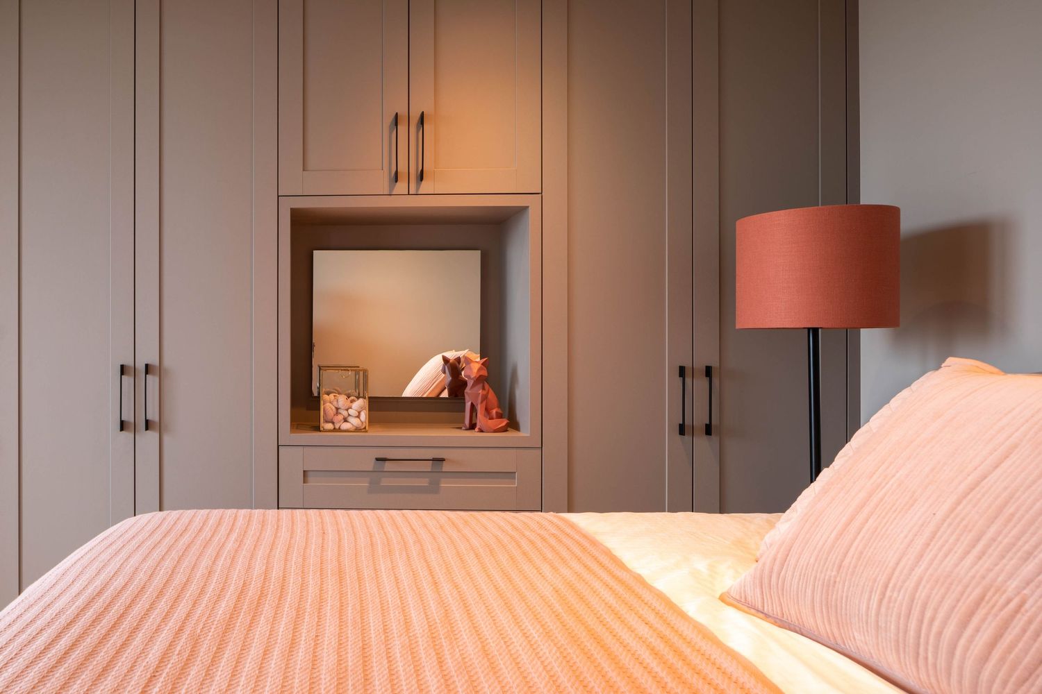 Modern gray kitchen cabinets with coral-colored pendant lights and gold hardware create a sleek contemporary design.