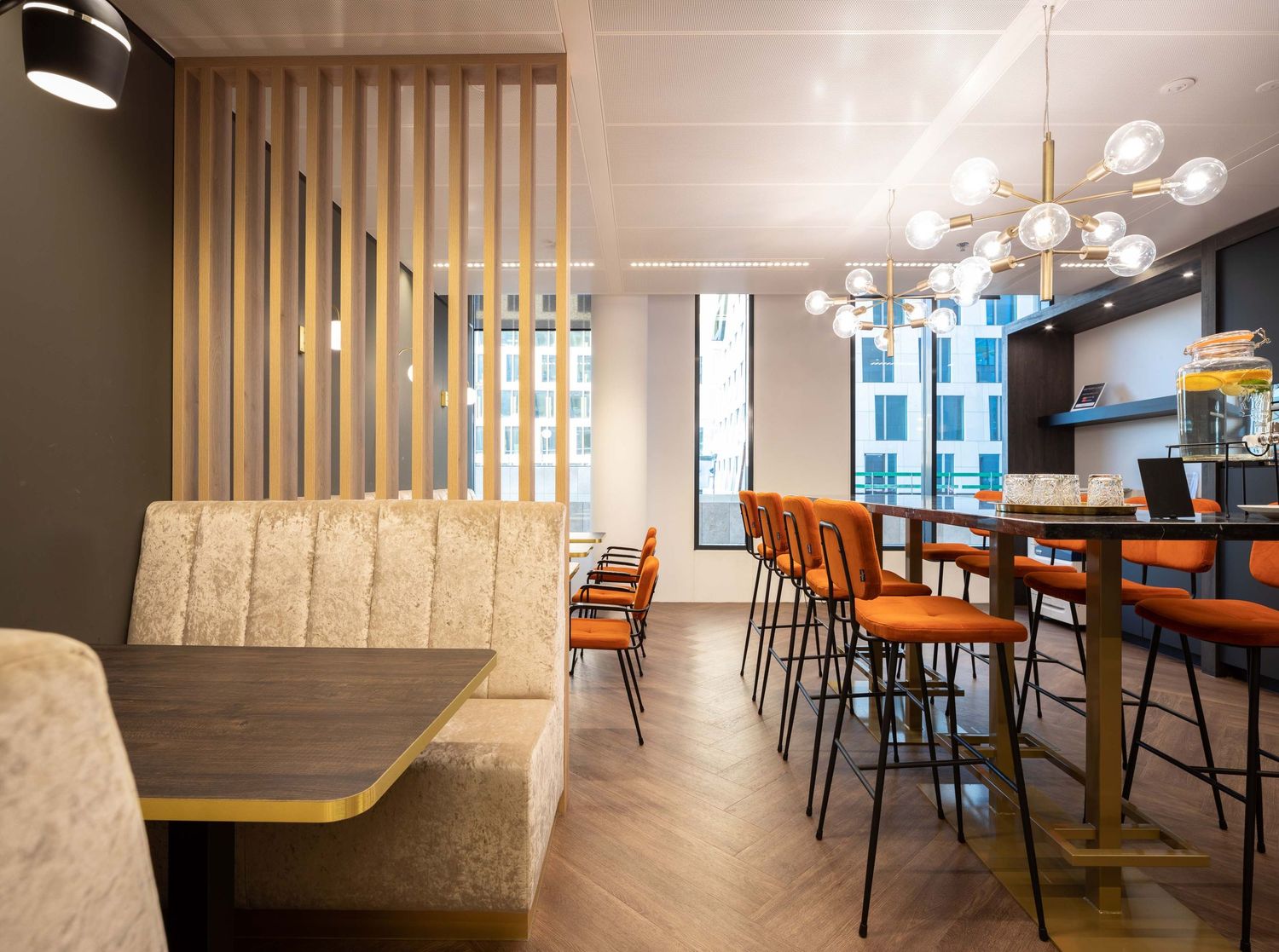 Modern restaurant interior with wooden slat dividers, orange chairs, and pendant lighting creates a warm contemporary atmosphere.
