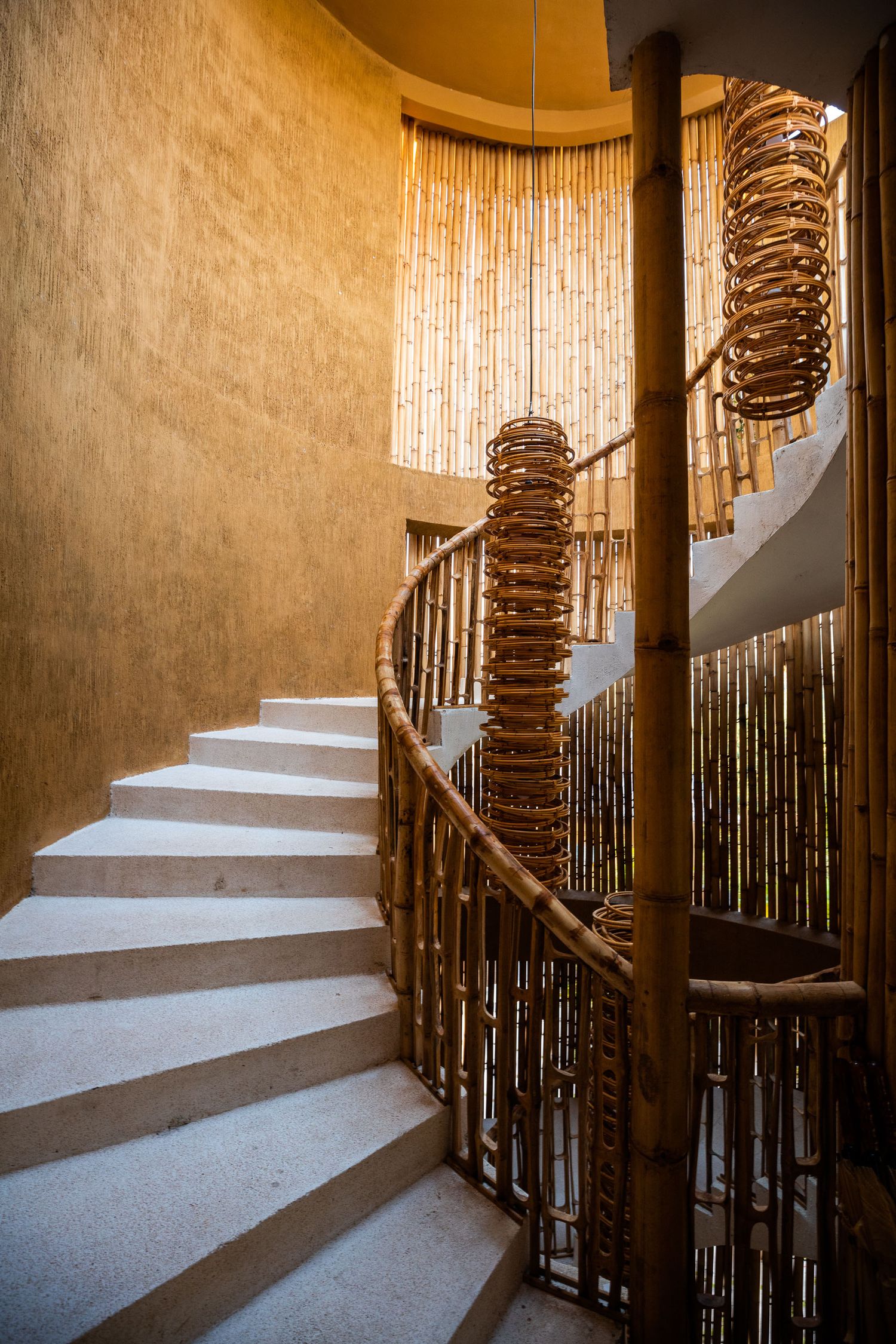 Spiral staircase with white steps and bamboo-style railing in warm lighting.