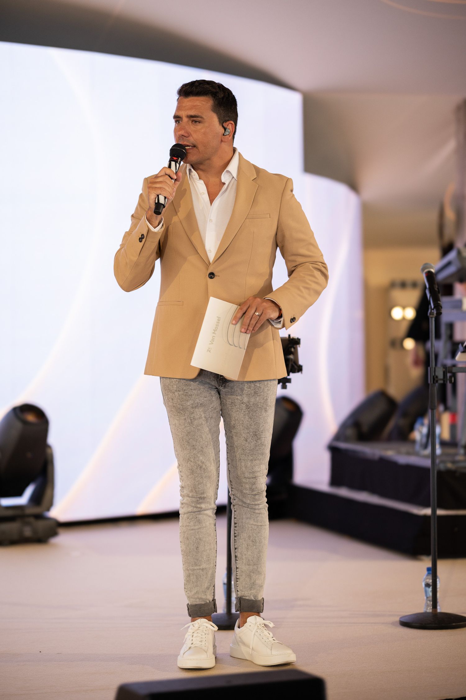 A performer in a beige blazer and light colored pants sings on stage in a series of sequential photos.