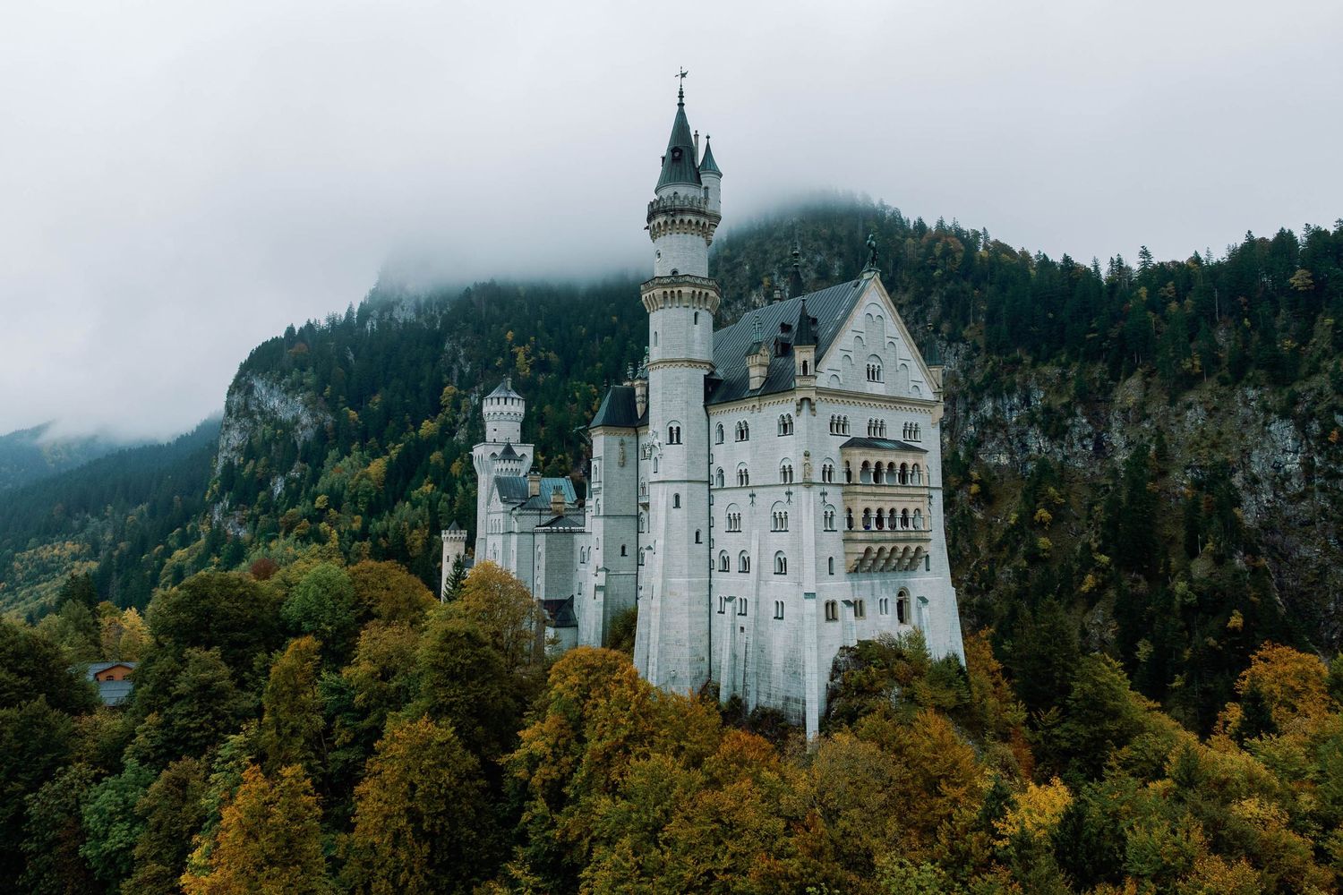 Neuschwanstein Castle rising above autumn forests with misty mountains in Bavaria, Germany.
