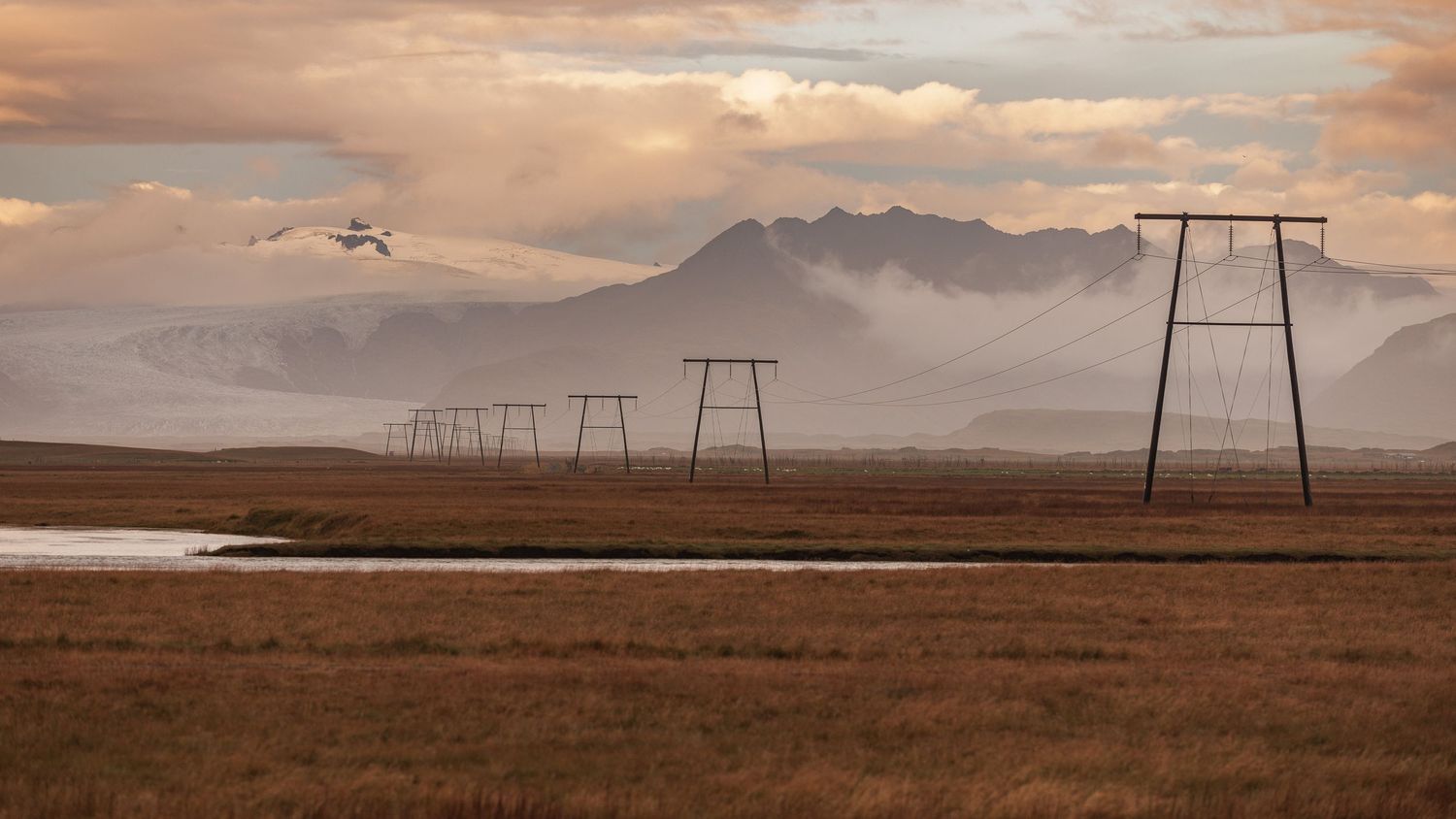 A panoramic view of power lines stretching across a vast desert landscape at sunset with mountains in the distance.