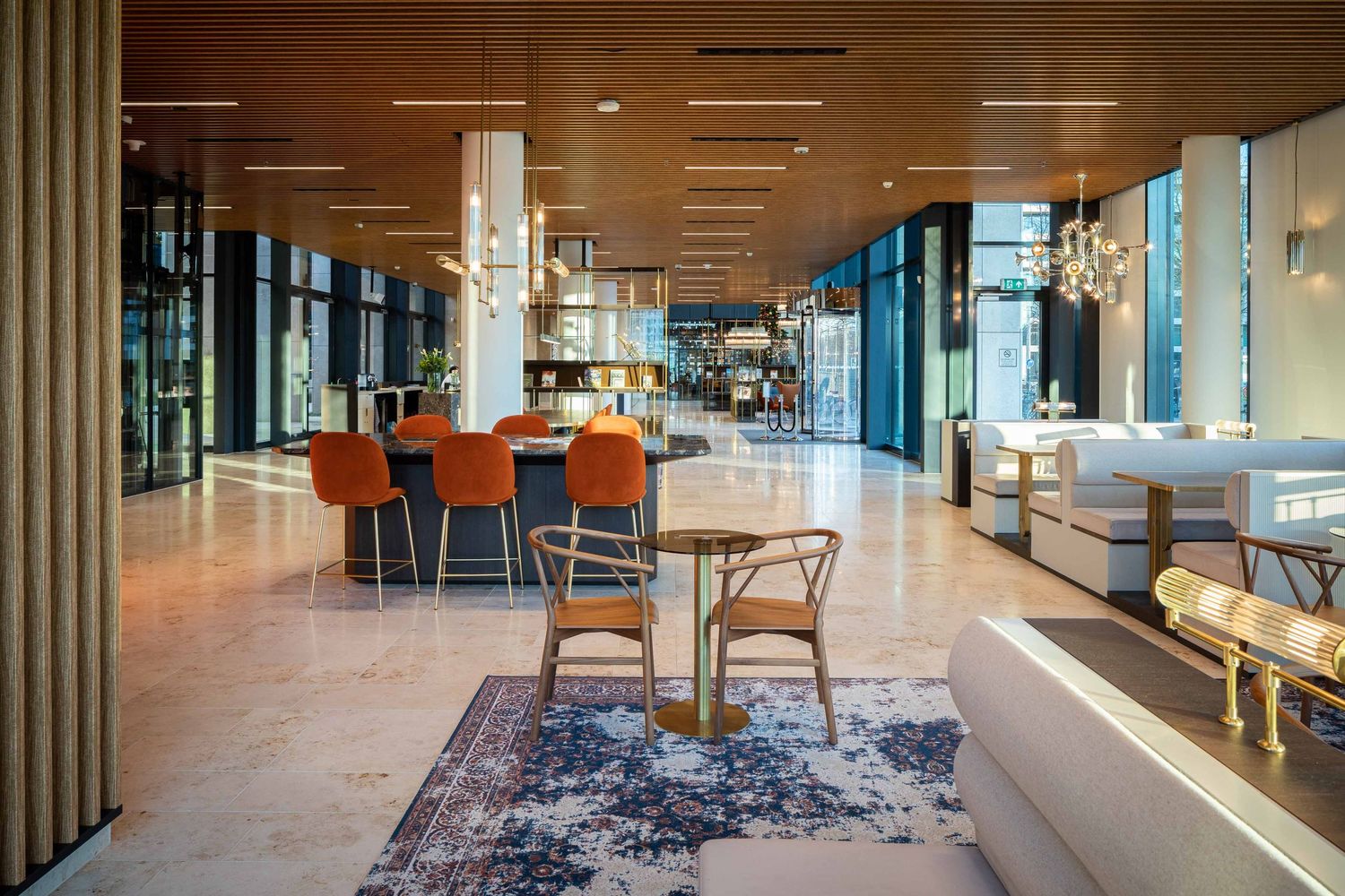 Modern office interior with wood floors, glass walls, and lounge seating areas illuminated by natural light.
