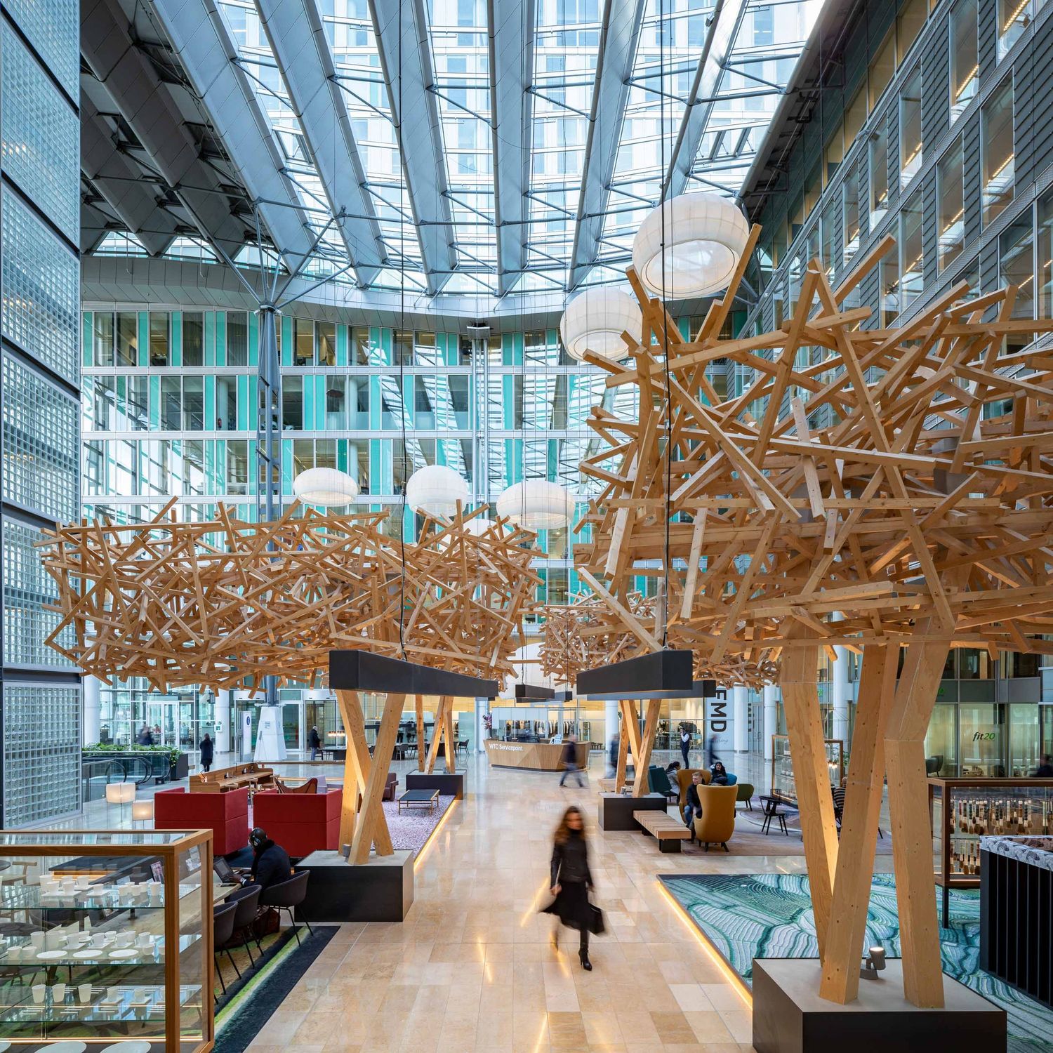 Modern office atrium with dramatic wooden sculptural installations suspended from glass ceiling and red seating below.