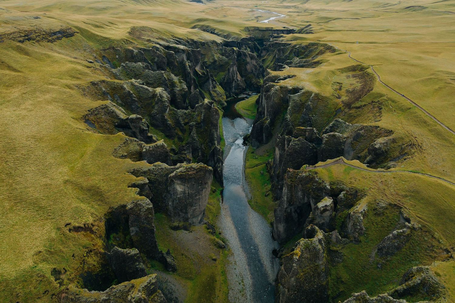 Aerial view of green valley with winding river cutting through dramatic cliffs.