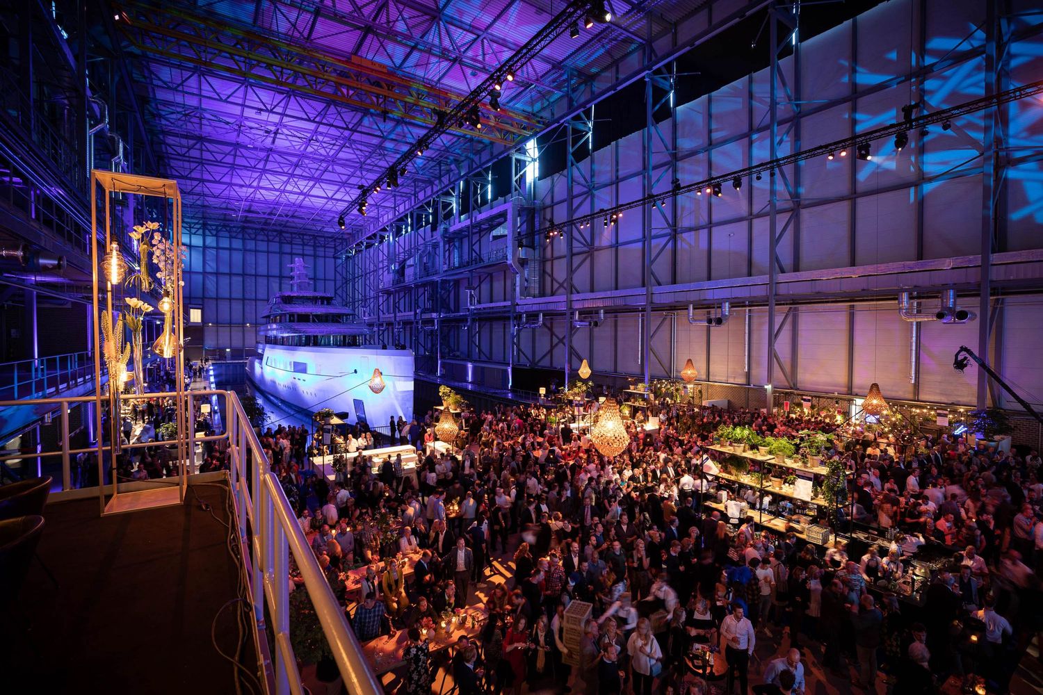 Large event venue illuminated with purple lighting shows crowd gathered for a corporate conference or presentation.