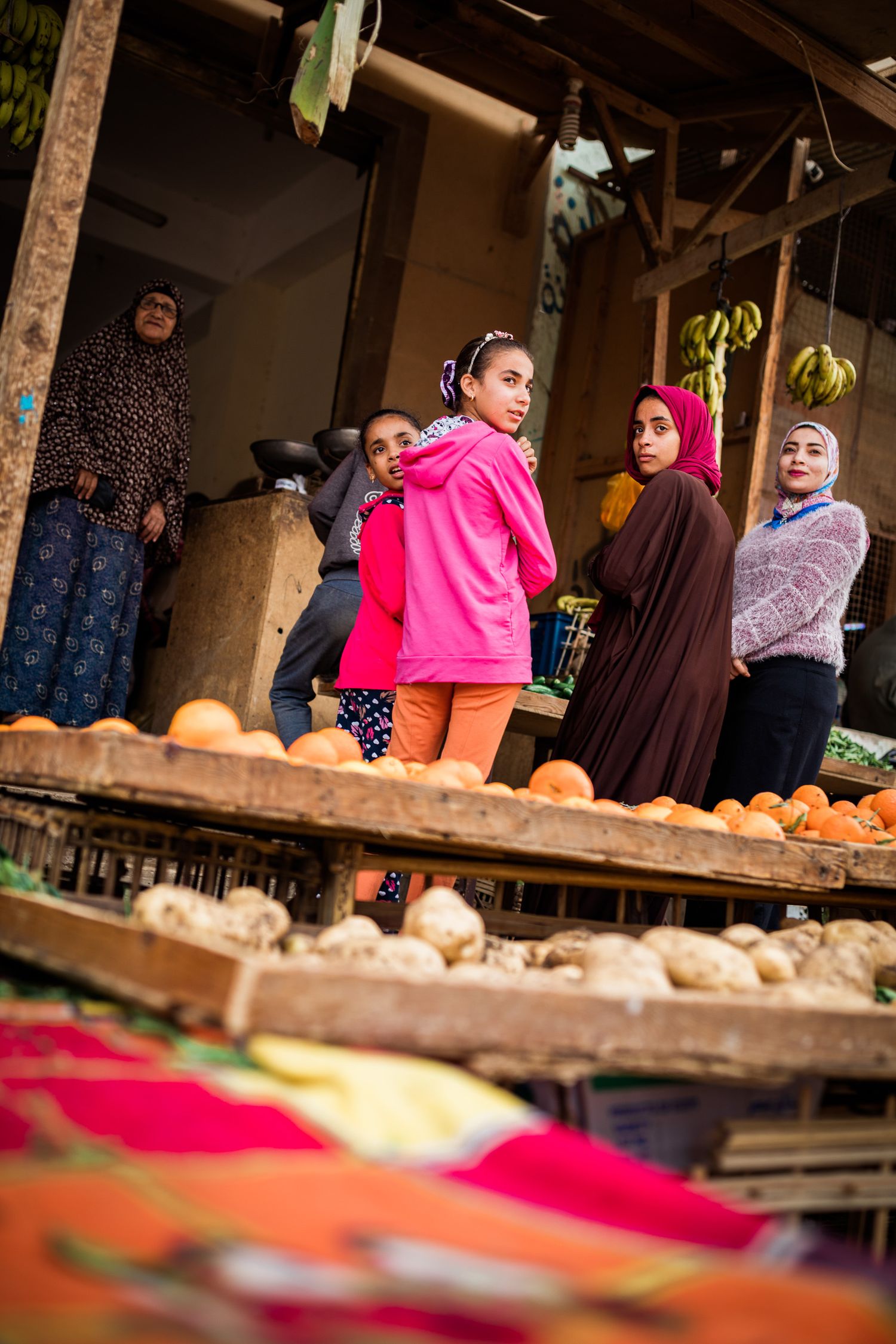 Market stall with colorful fabrics and produce on display under wooden beams.