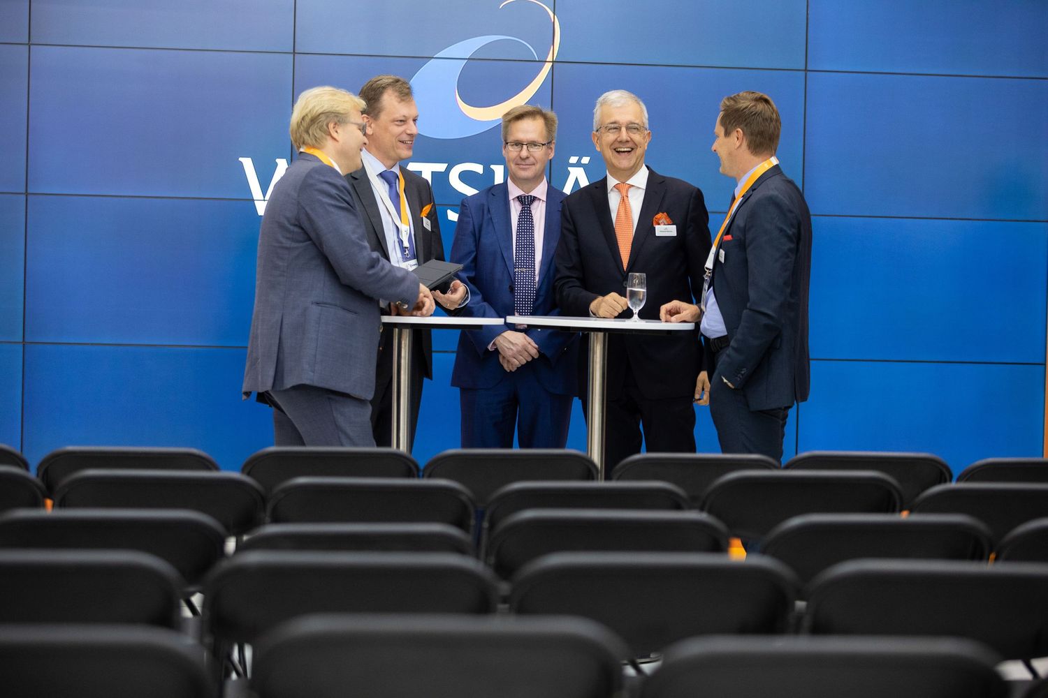 Business executives in suits having a discussion in front of a bright blue wall during a professional meeting.