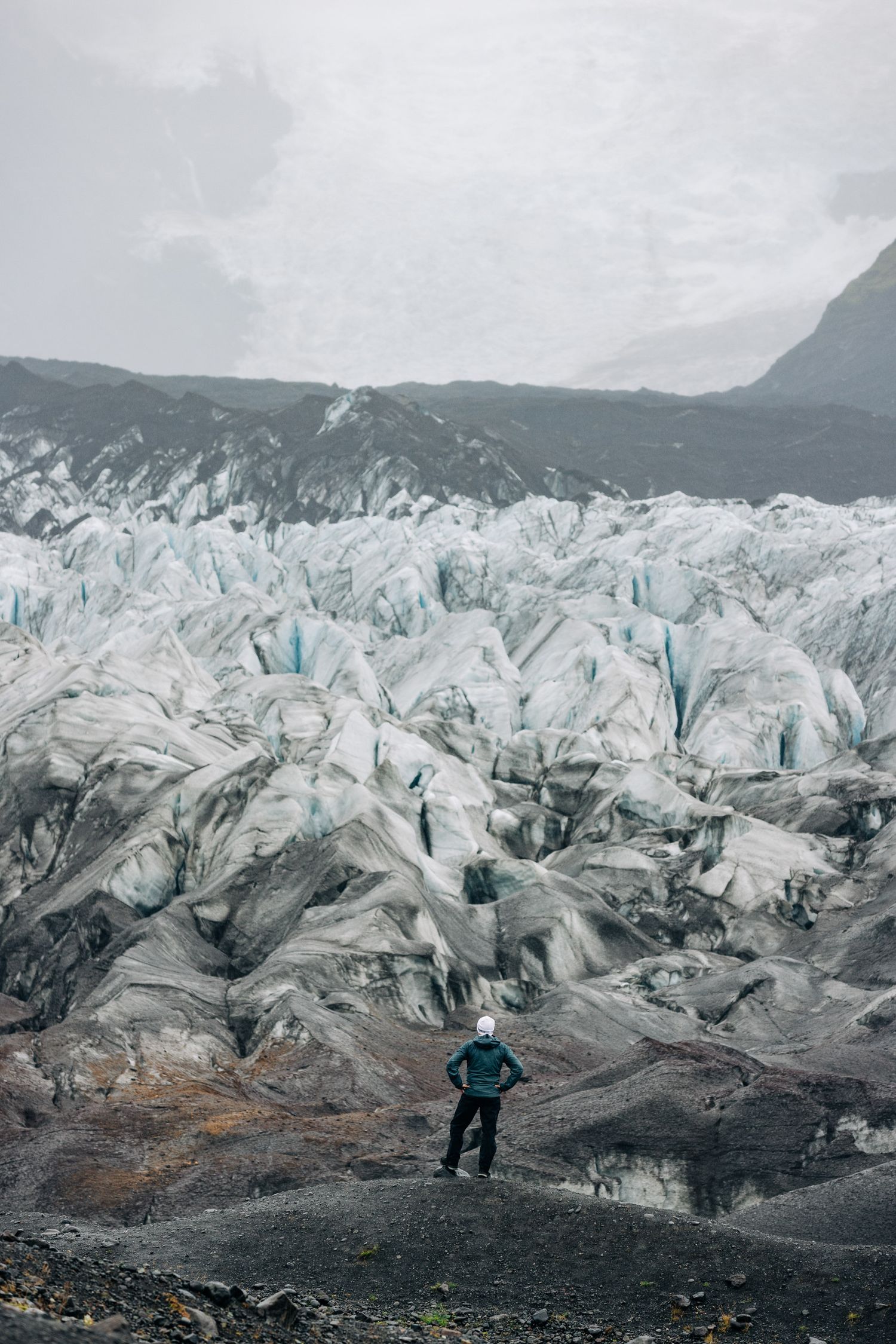 Panoramic view of a rugged glacier landscape with jagged ice formations and rocky terrain in muted grey tones.
