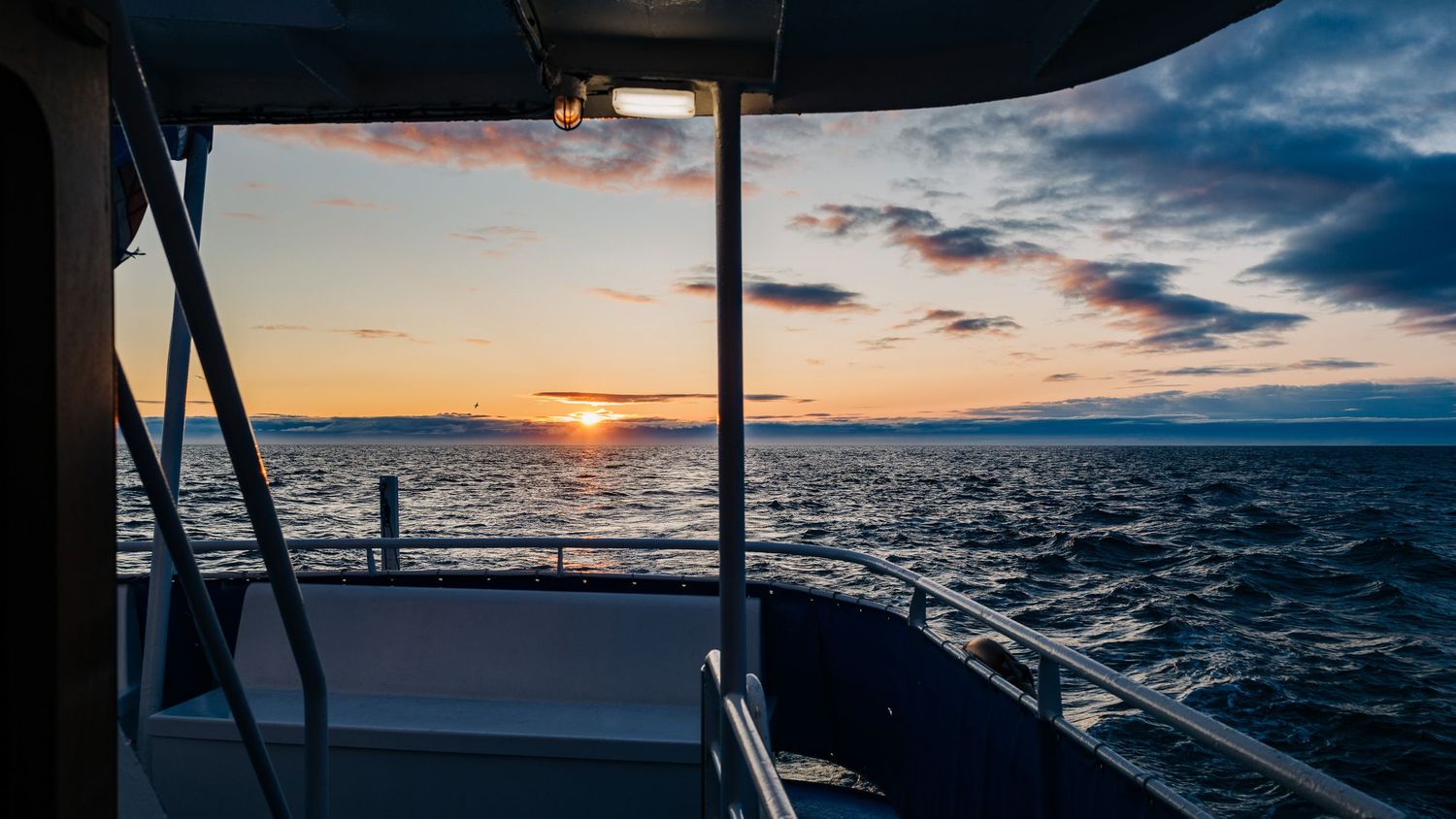 Panoramic sunset view over the ocean with dramatic clouds and sun rays breaking through on the horizon.