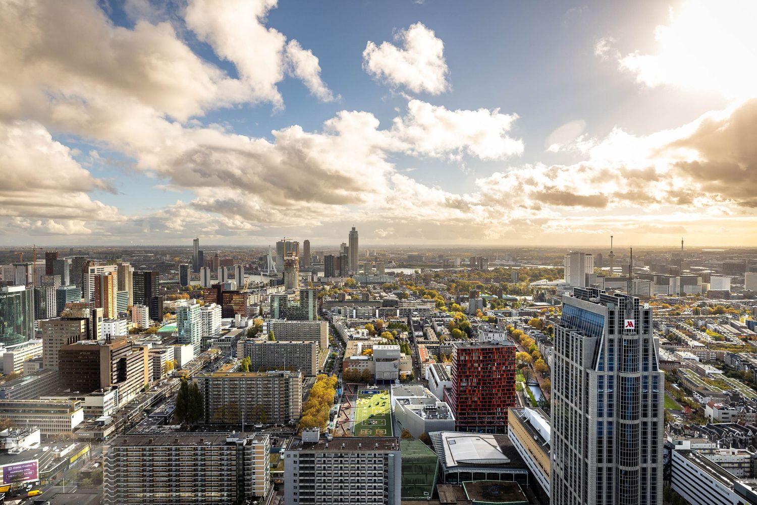 Aerial panoramic view of a modern city skyline under dramatic cloudy sky with golden sunlight at dusk.