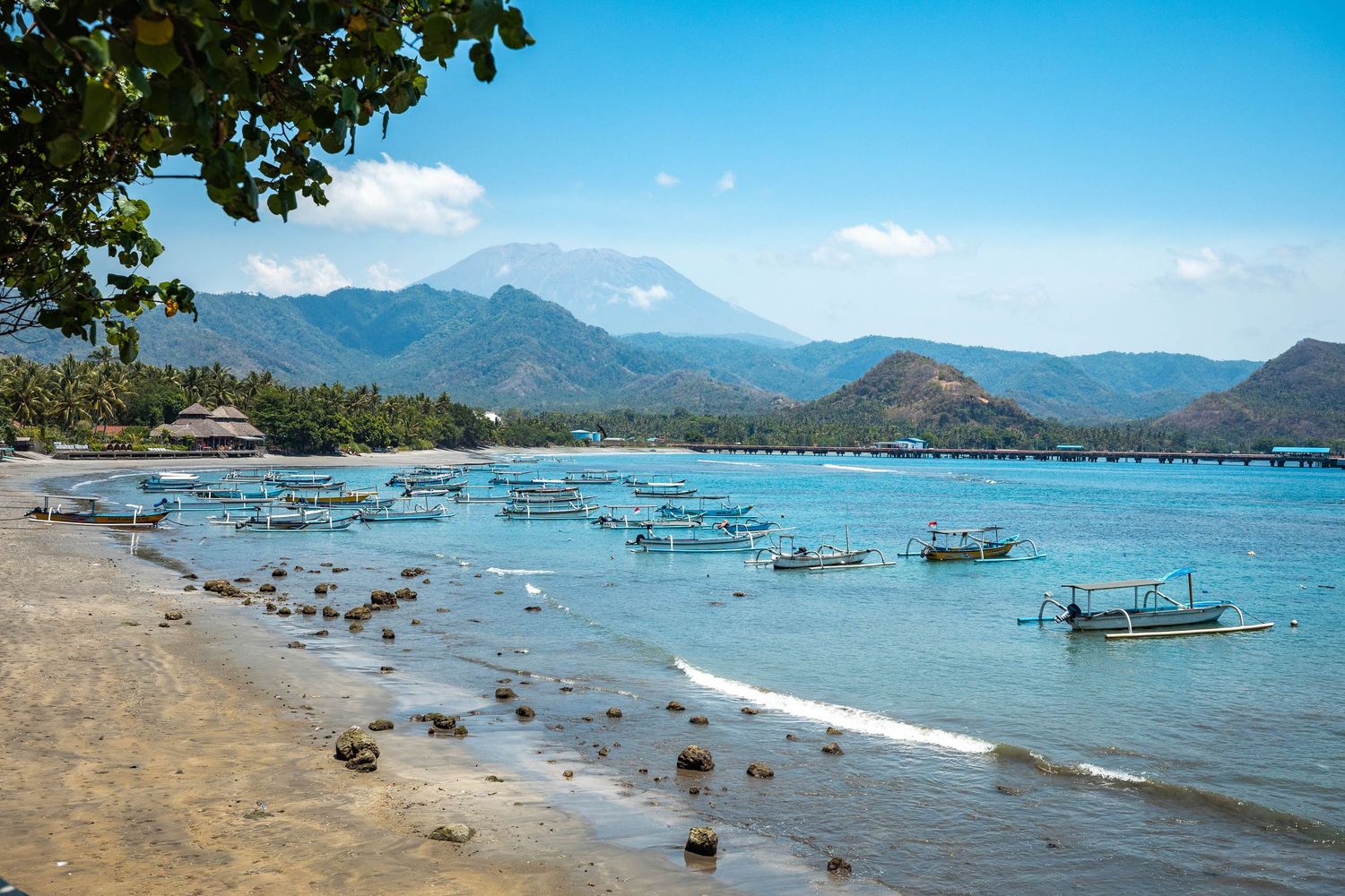 Panoramic view of a tropical bay with traditional fishing boats anchored in turquoise waters against mountain backdrop.