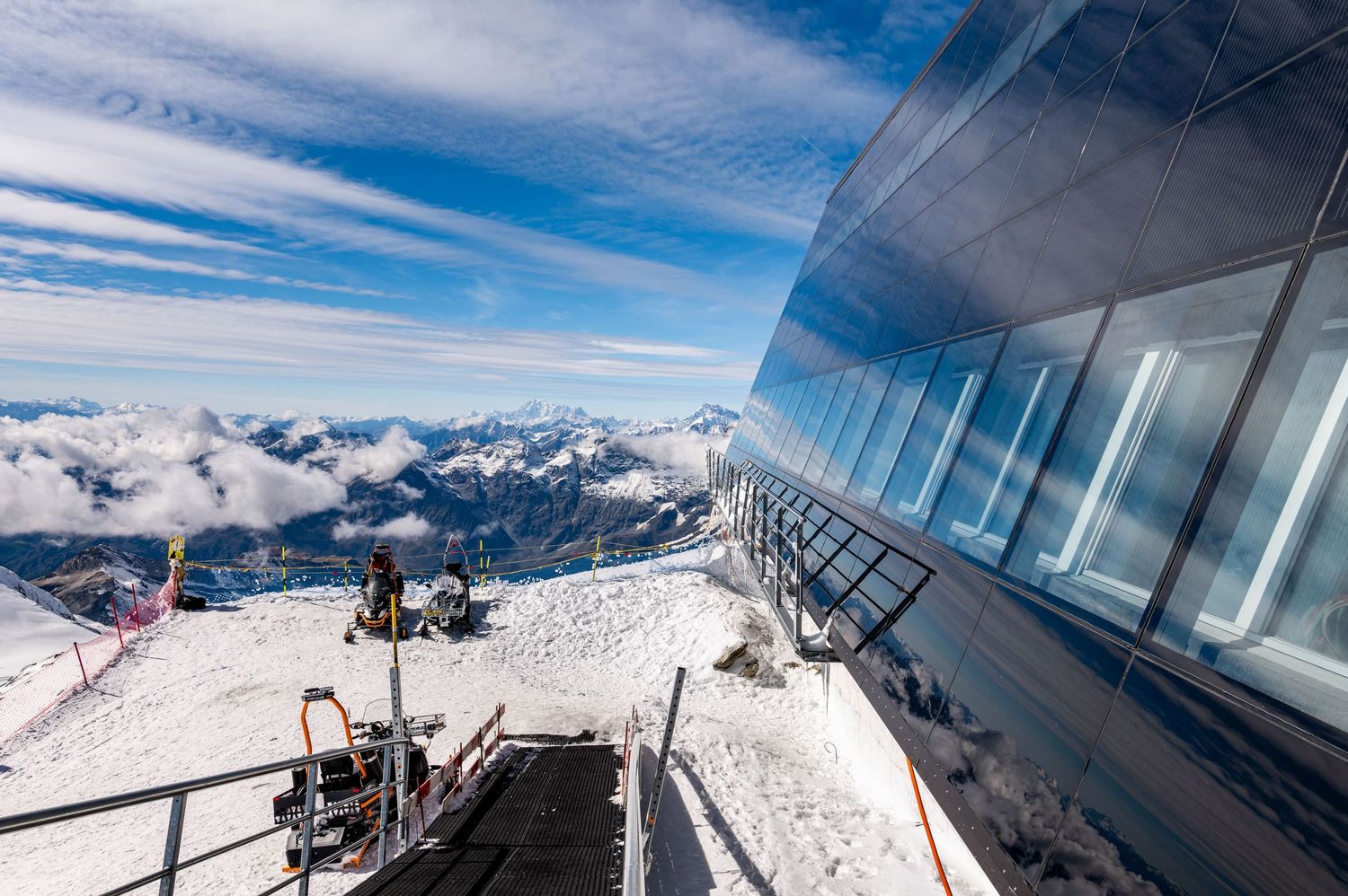 Panoramic viewing platform with metal railings on a snow-covered mountain summit.