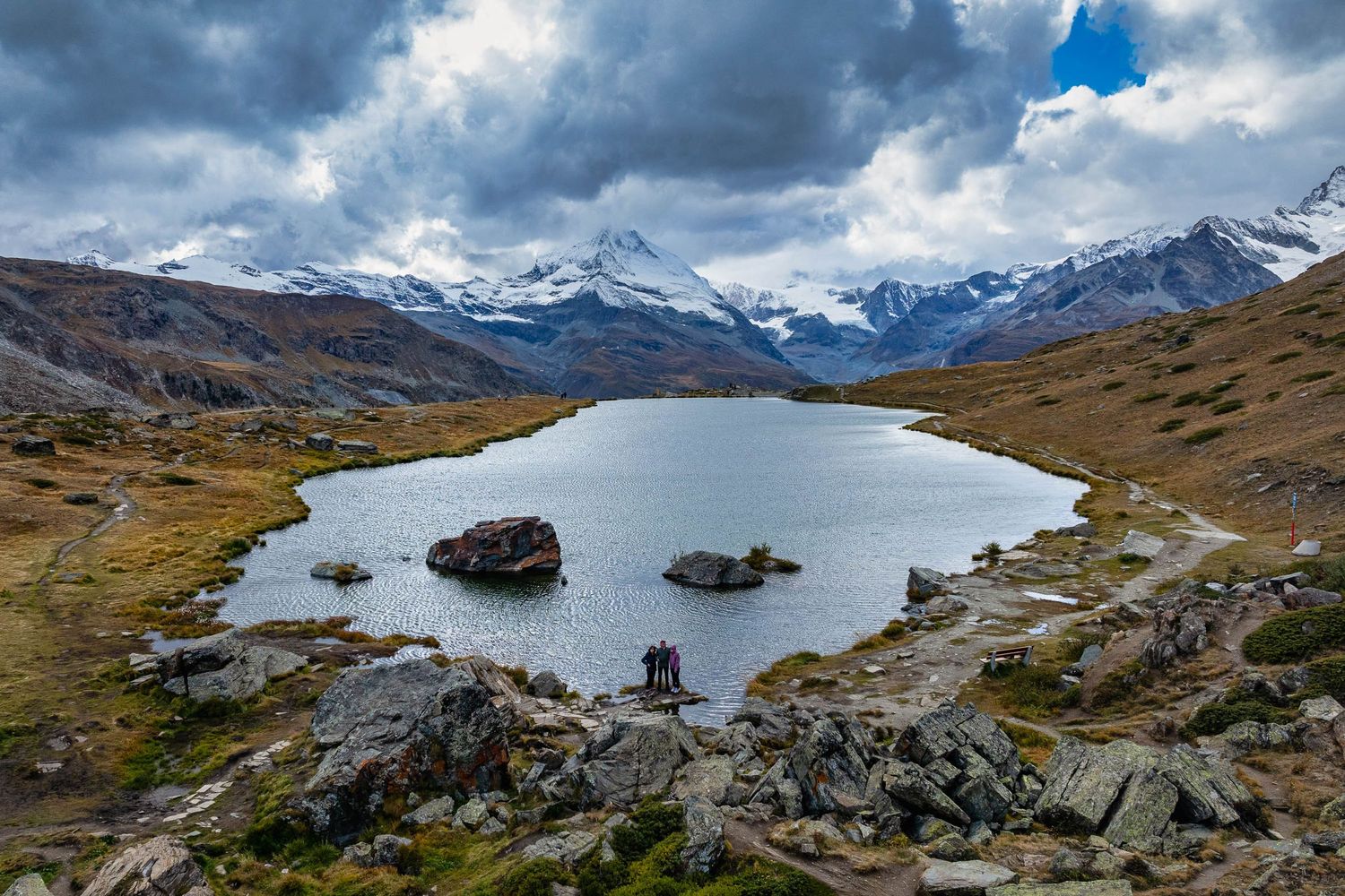 Snow-capped mountain peaks reflect in an alpine lake surrounded by rocky terrain.