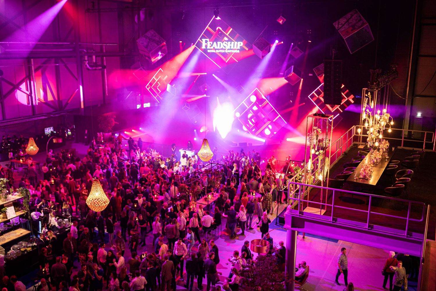 Crowded nightclub dance floor illuminated by vibrant purple lighting and special effects during a party event.