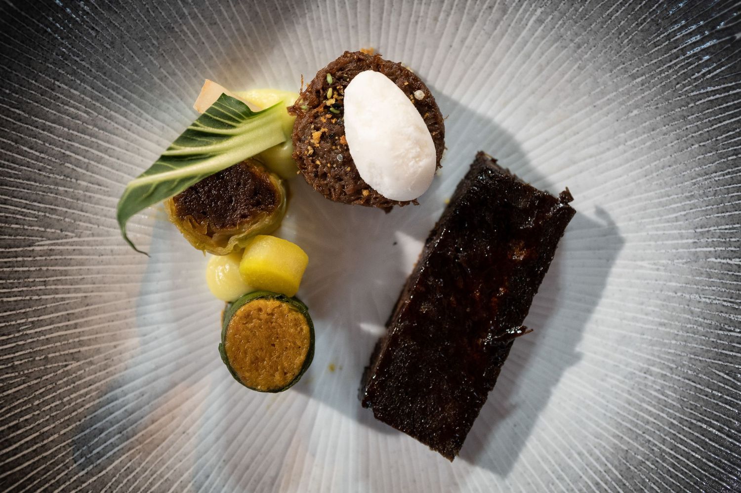 Dark chocolate brownie garnished with fresh mint leaf and powdered sugar on a modern black plate.