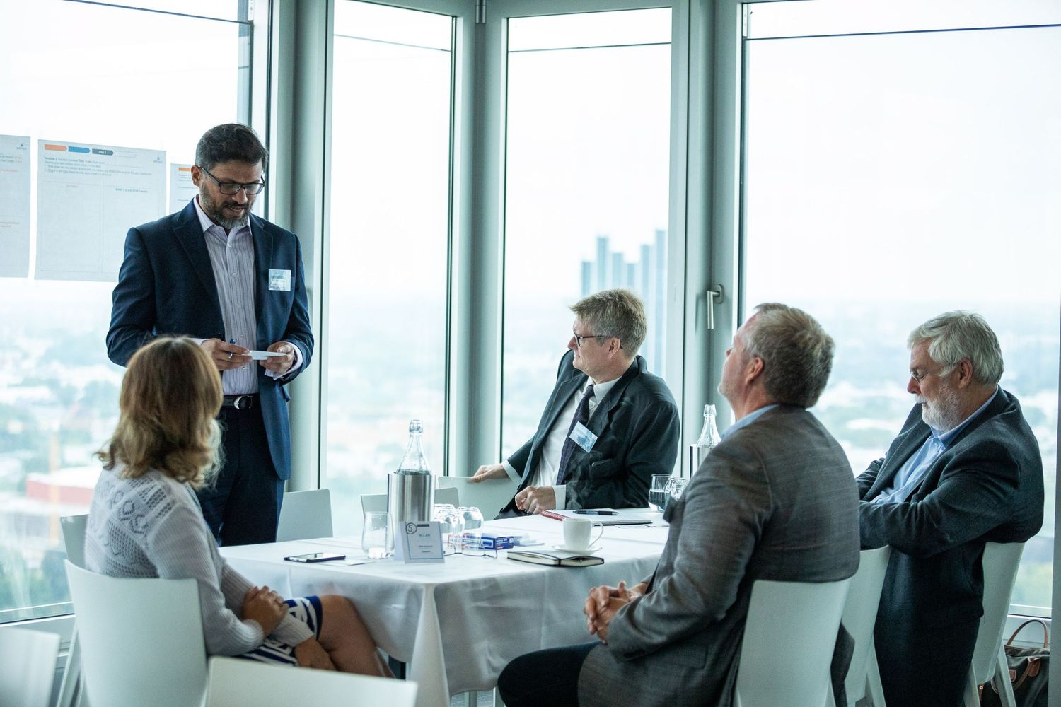 Corporate meeting taking place in a bright office space with city views through large windows.