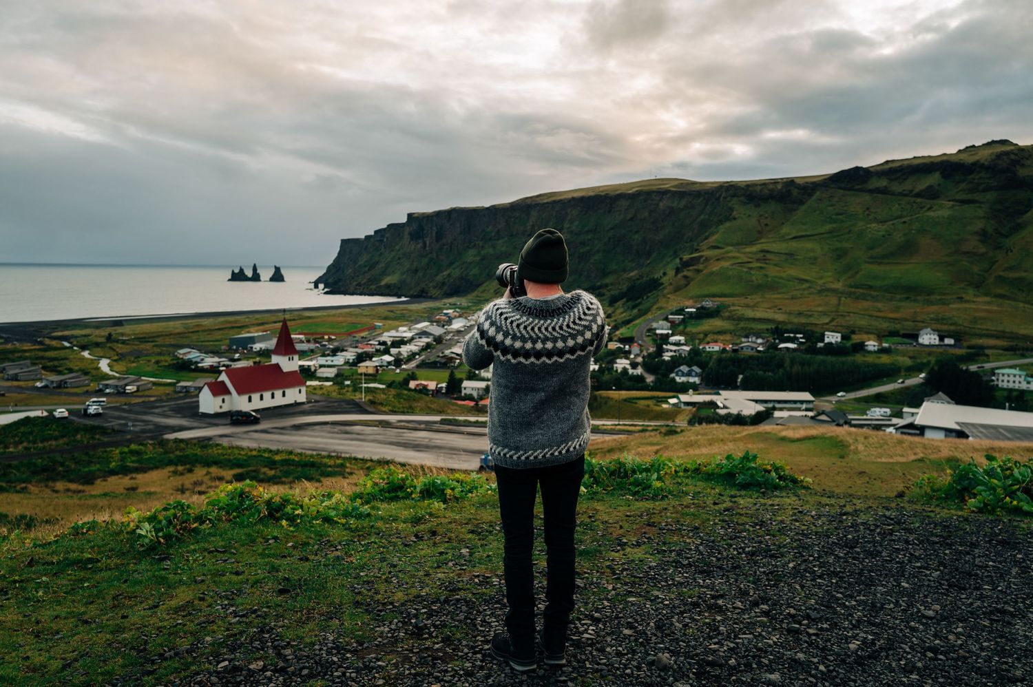 Panoramic view of Vik's black sand beach in Iceland with dramatic cloudy skies and coastal cliffs.