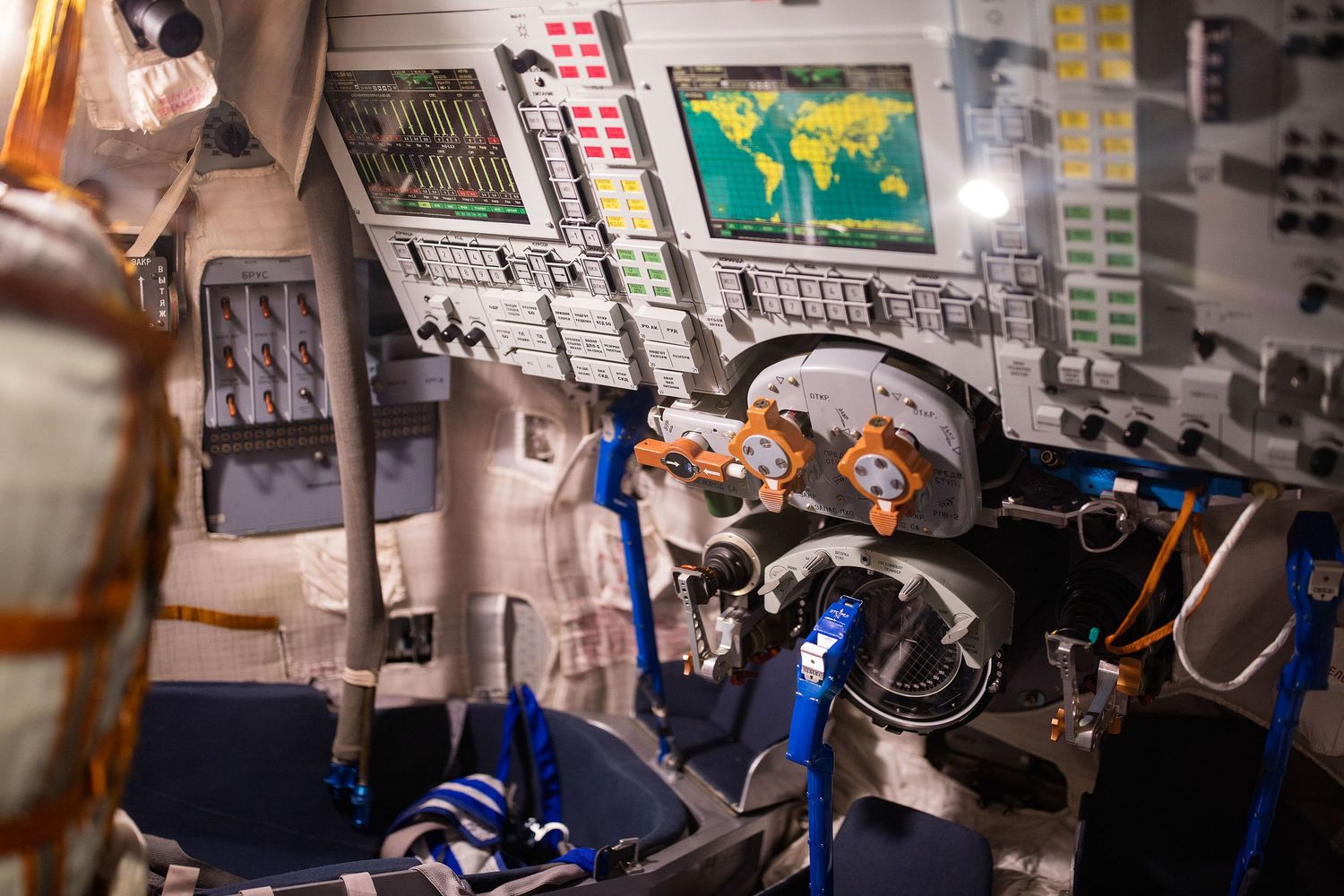 Interior view of a spacecraft cockpit with control panels, monitors displaying a world map, and complex wiring systems.