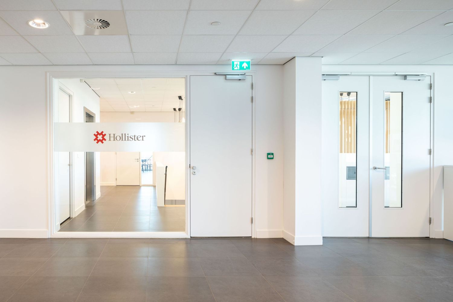 Long white hallway with fluorescent lighting and multiple doorways in a modern office or medical building interior.