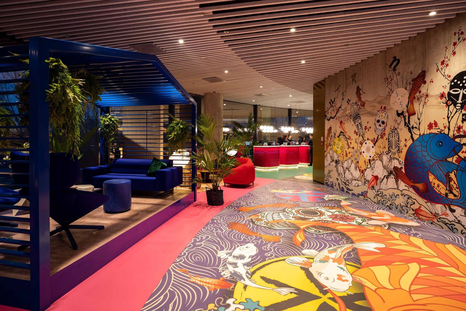 Modern restaurant interior with vibrant pink floor, artistic wall murals, and blue architectural elements.