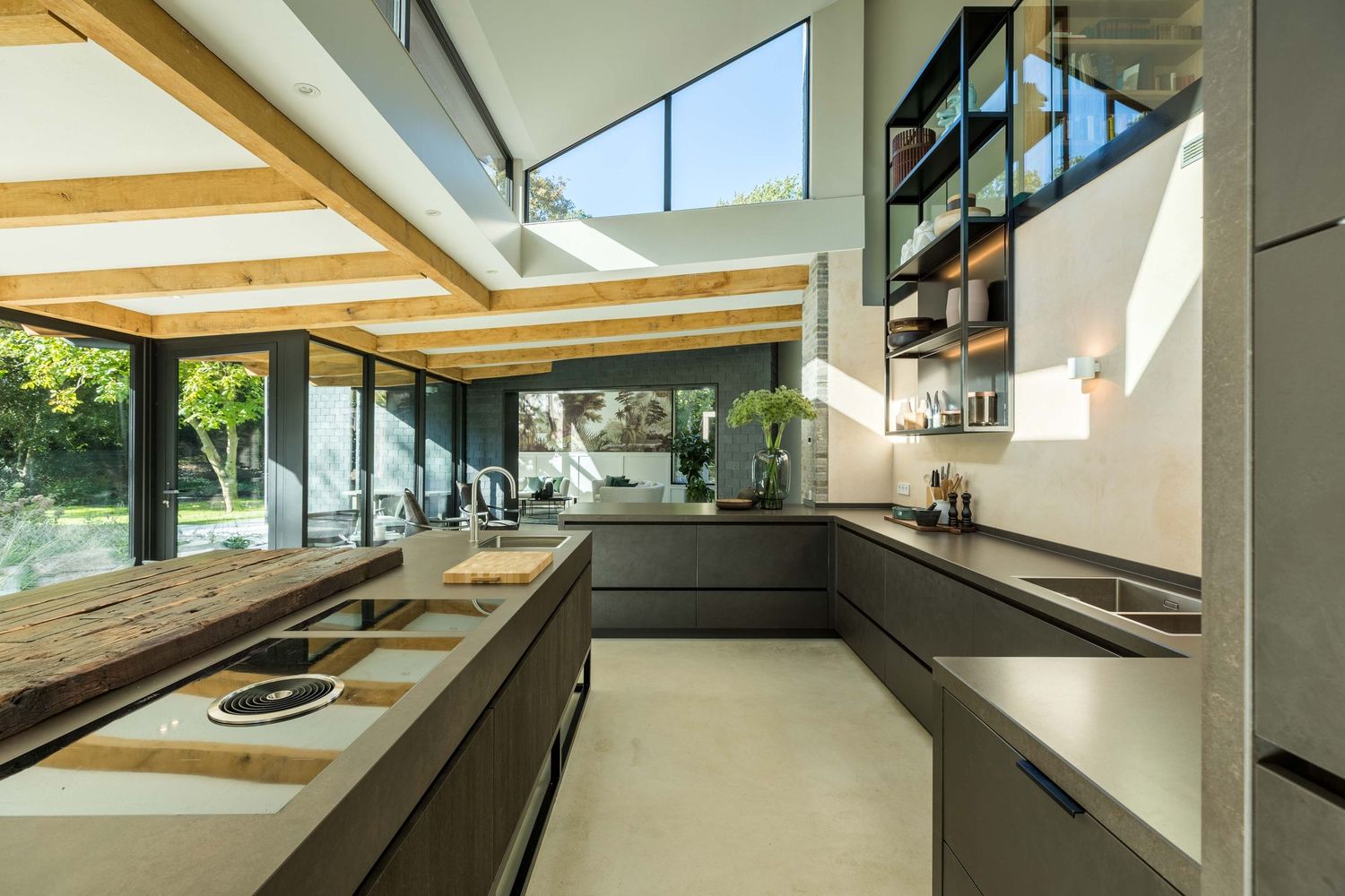 Modern kitchen with angled windows and skylights features sleek black countertops and wooden ceiling beams.