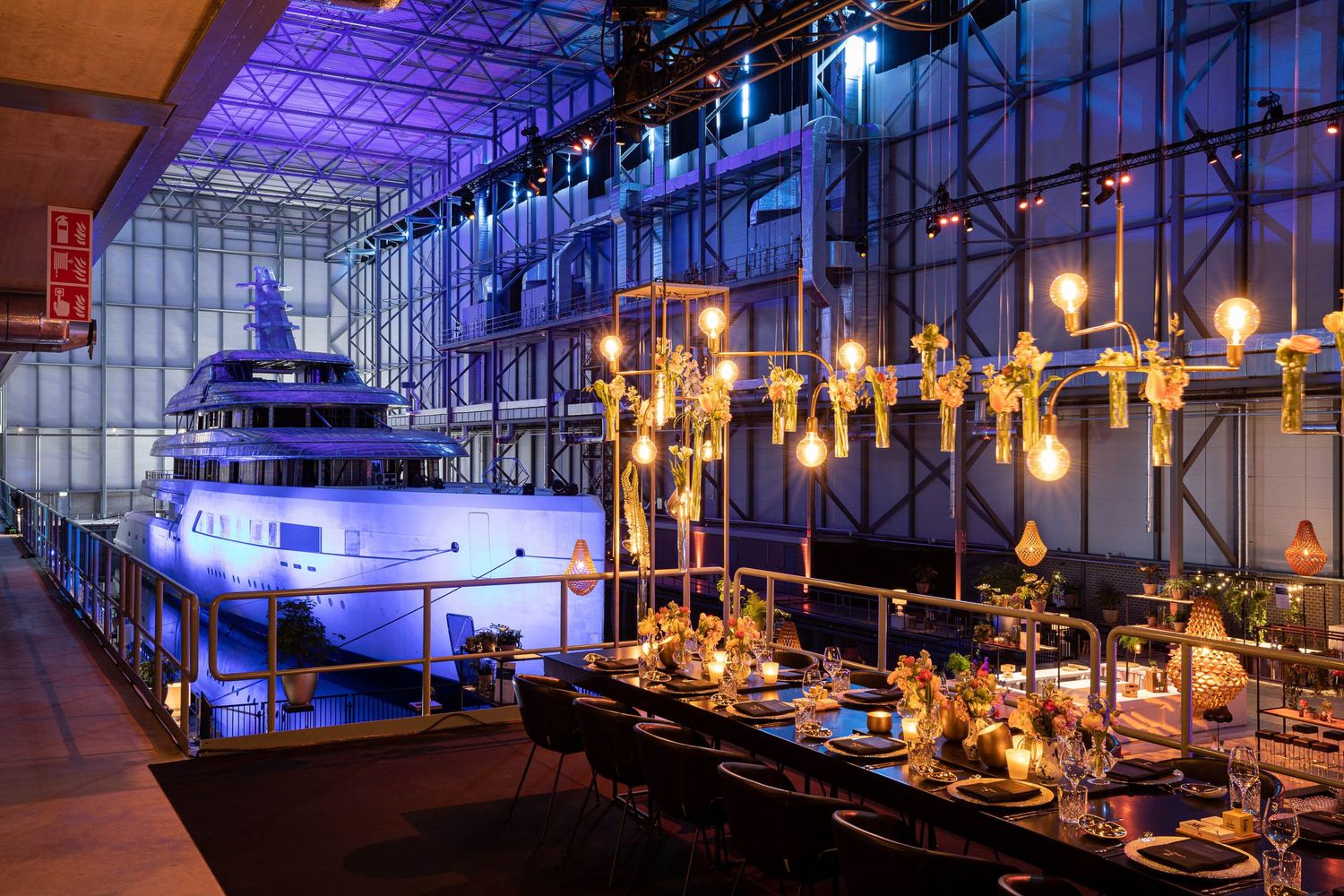 Luxury yacht displayed in indoor venue with elegant dining setup and dramatic blue lighting for special event.