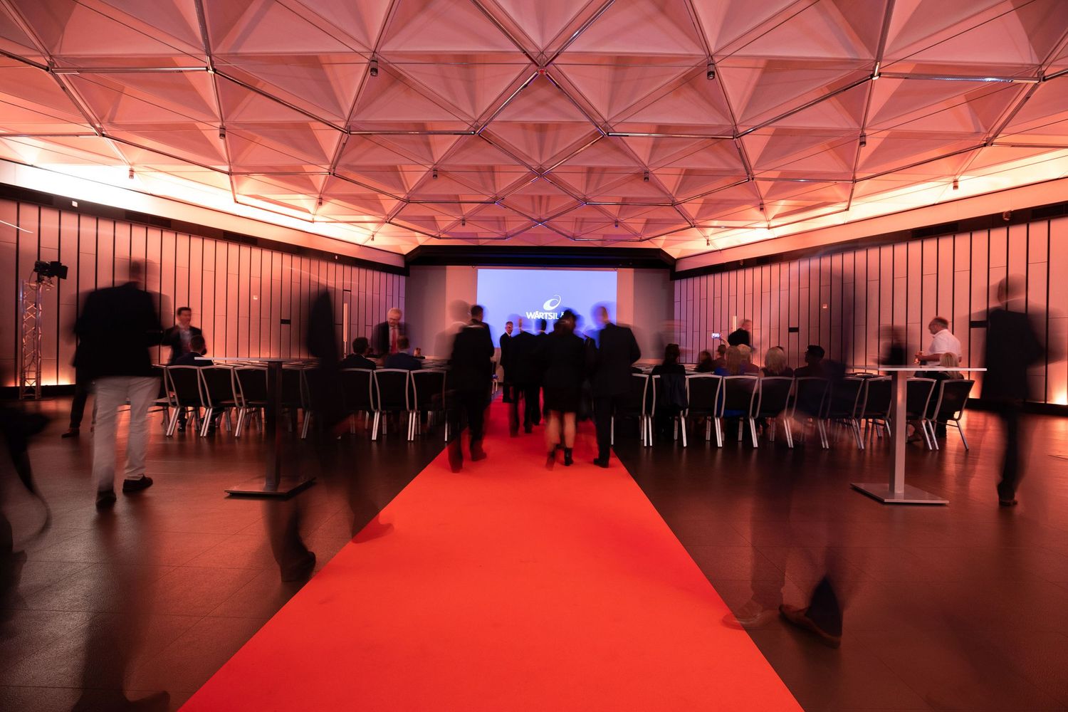 A geometric red-lit ceiling creates a dramatic architectural pattern in a modern event space.