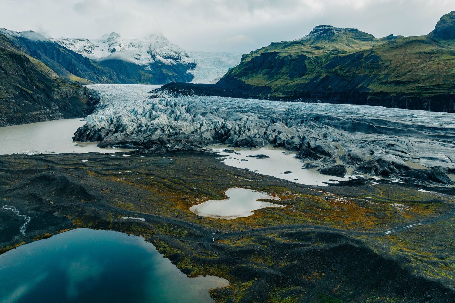 Panoramic view of a massive glacier descending from snow-capped mountains into a valley with moraine lakes.