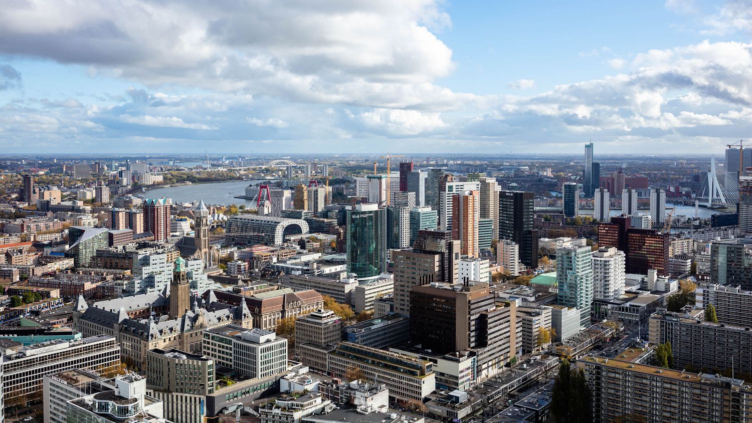 Aerial panoramic view of Rotterdam cityscape with modern skyscrapers, river, and partly cloudy sky.