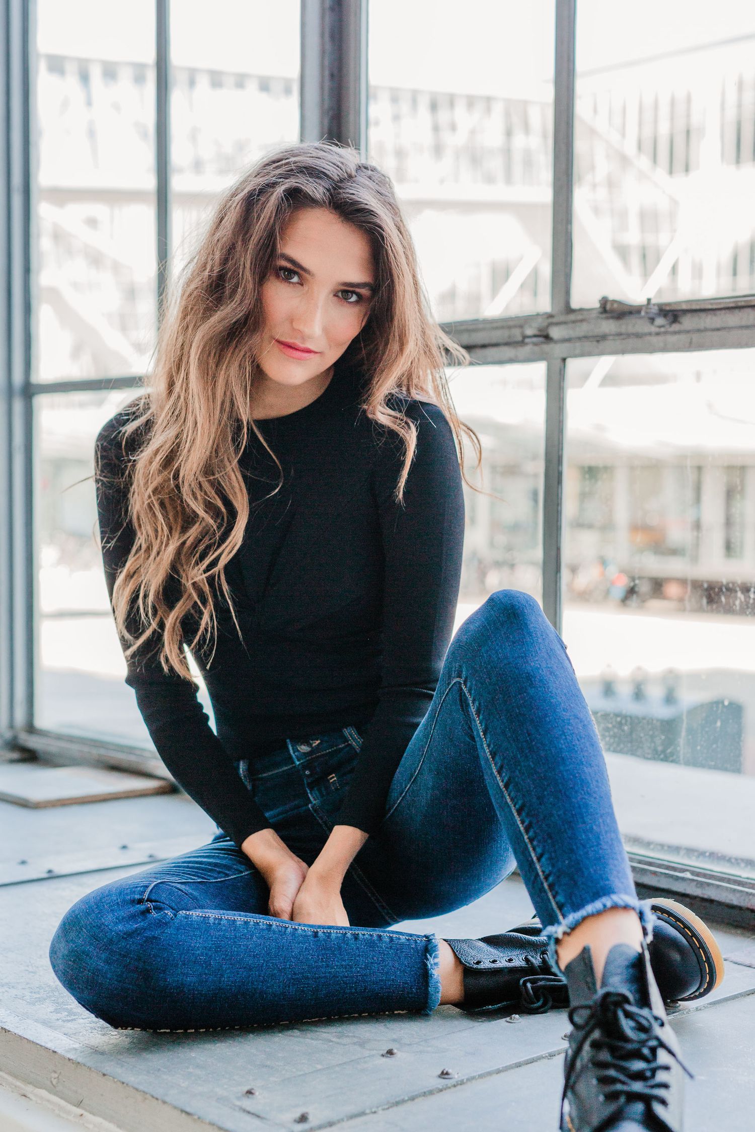 Fashion portrait series showing casual style with black sweater, jeans and boots against an industrial window backdrop.
