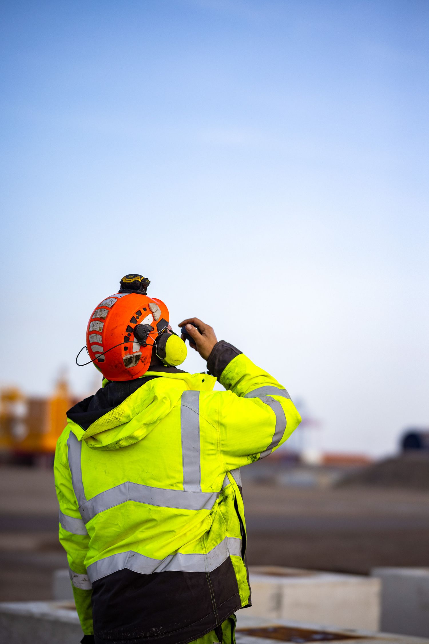 Worker in high visibility gear observing construction at an offshore wind facility.
