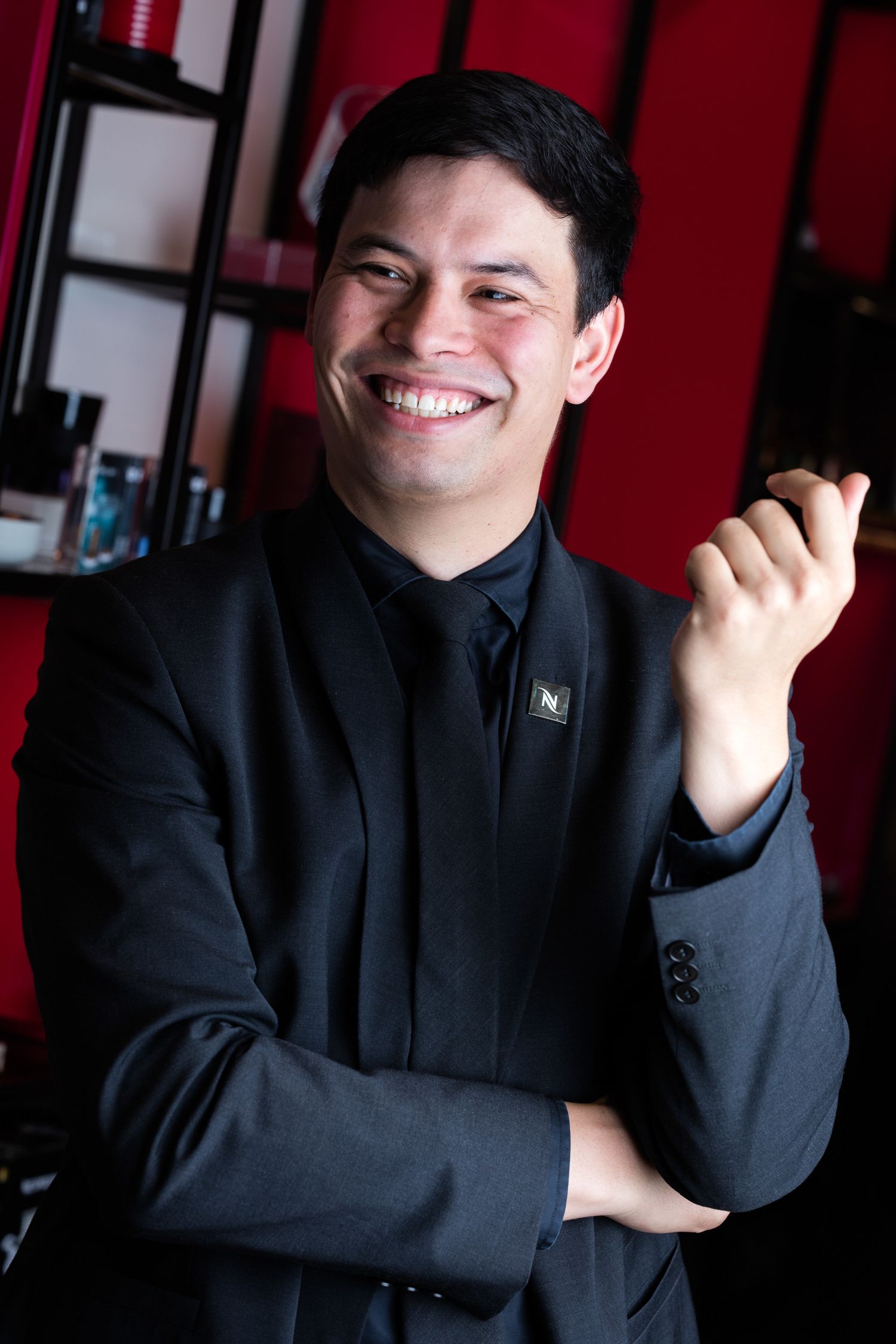 Person in black attire gesturing enthusiastically against red background.