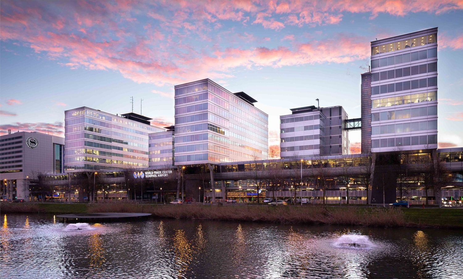 Modern office buildings reflecting pink sunset clouds in waterfront location.