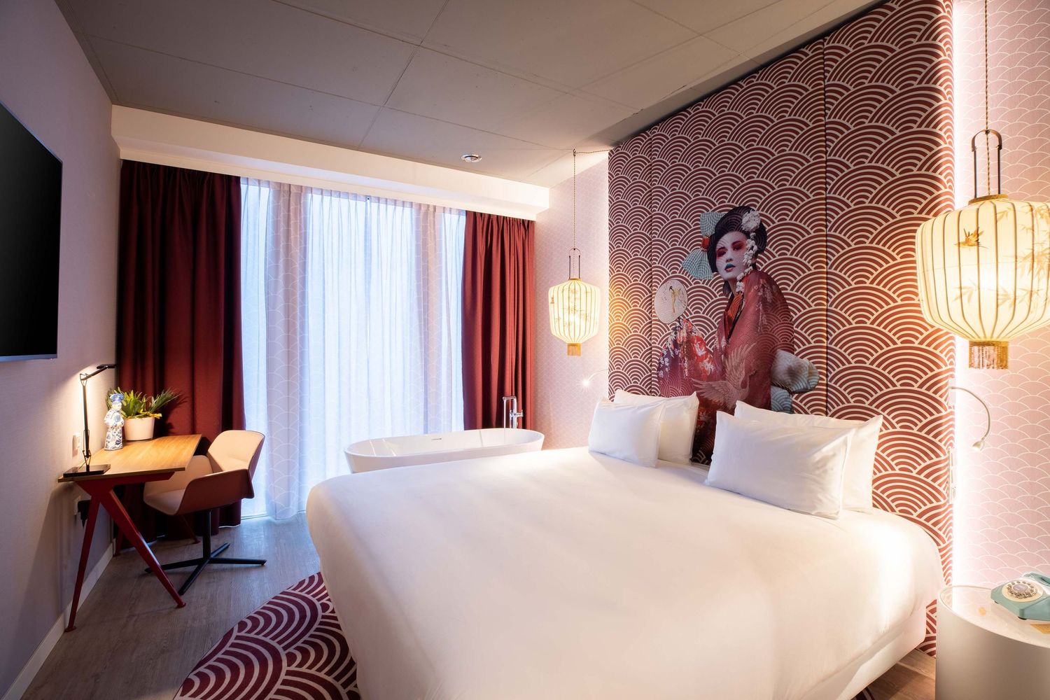 Modern hotel room with geometric patterned wallpaper, white bedding, red curtains, and decorative Asian-inspired wall art.