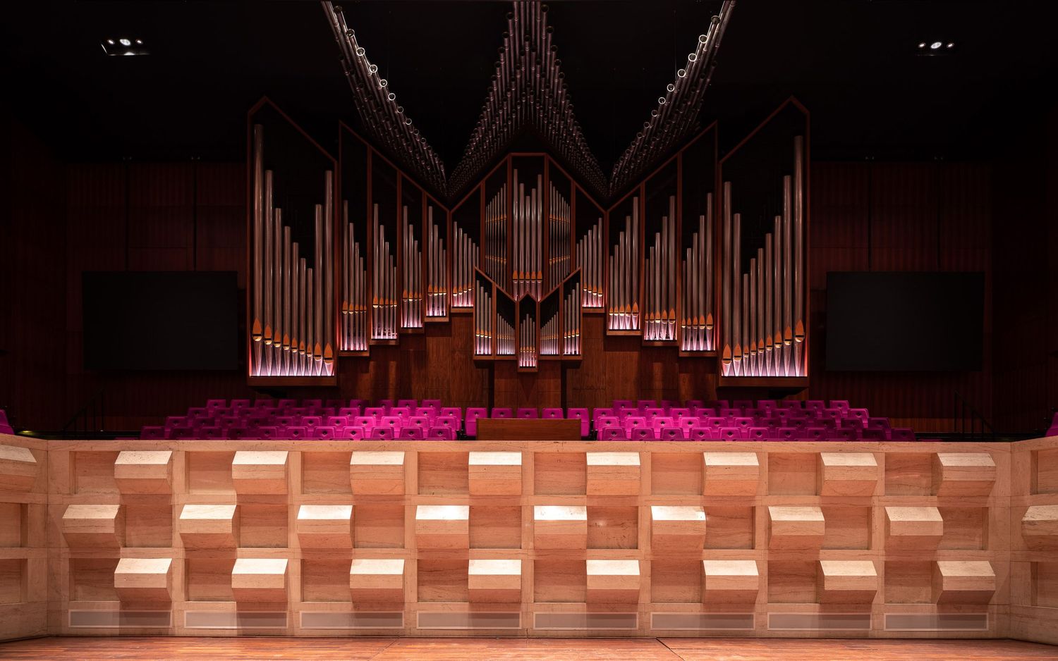 Interior view of a grand concert hall with wooden paneling and rows of organ pipes illuminated in warm lighting.