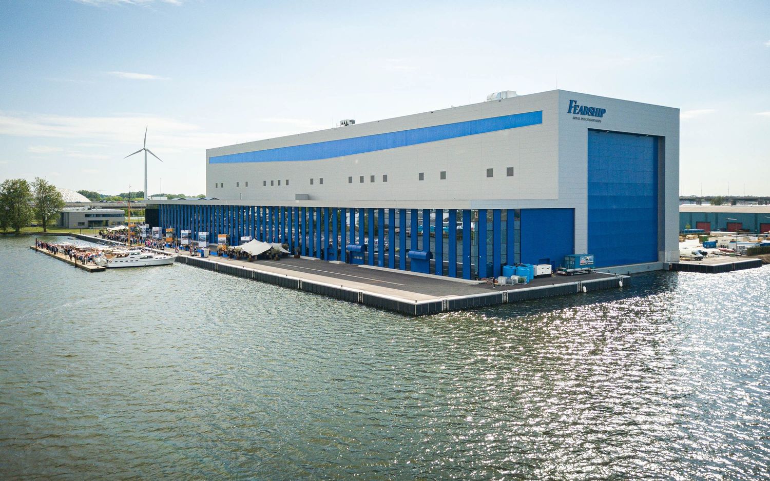 A modern blue and white floating warehouse facility on a waterfront with multiple boat docks and loading areas.