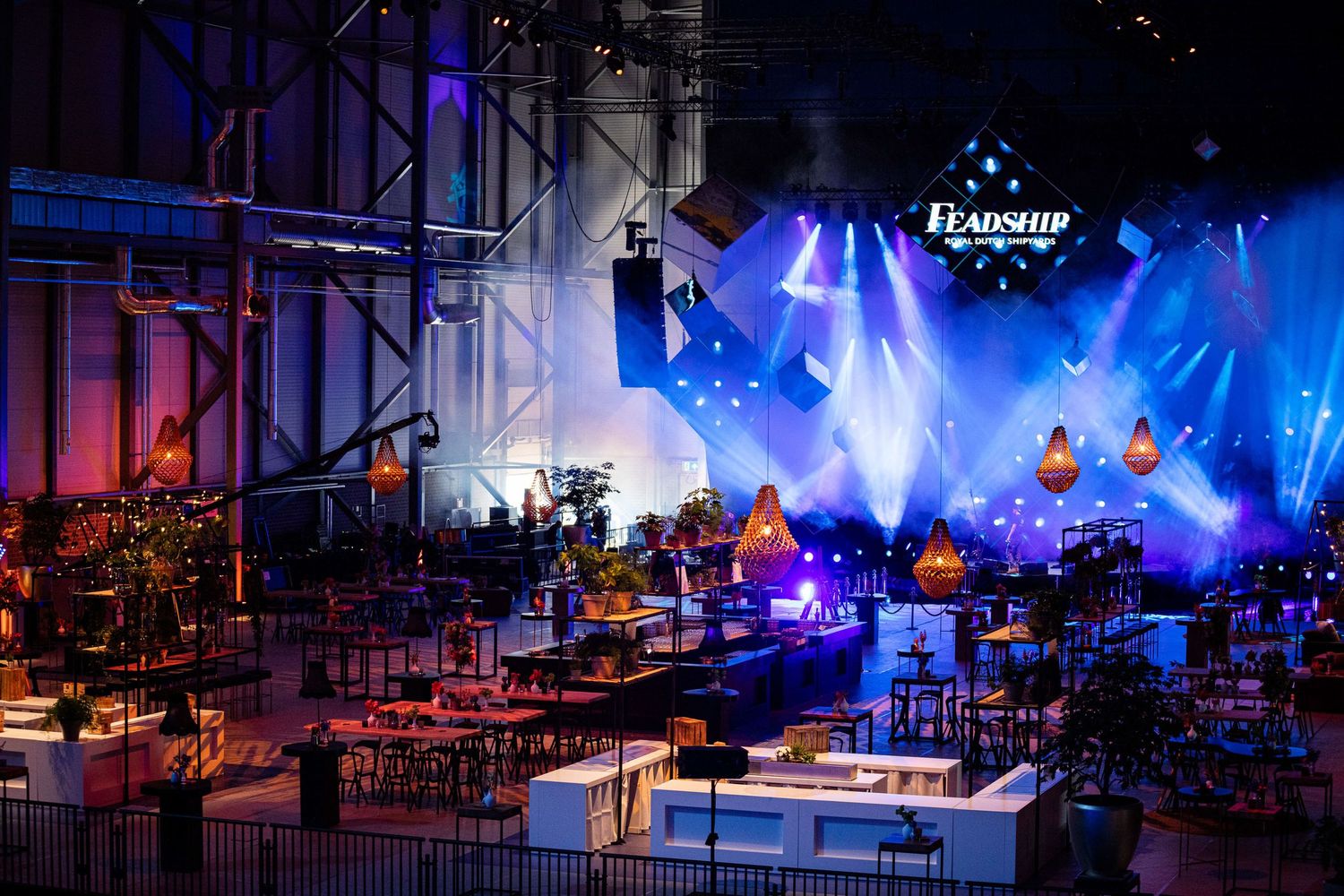 Concert venue with tables and chairs set up under dramatic blue stage lighting and performance rigging.