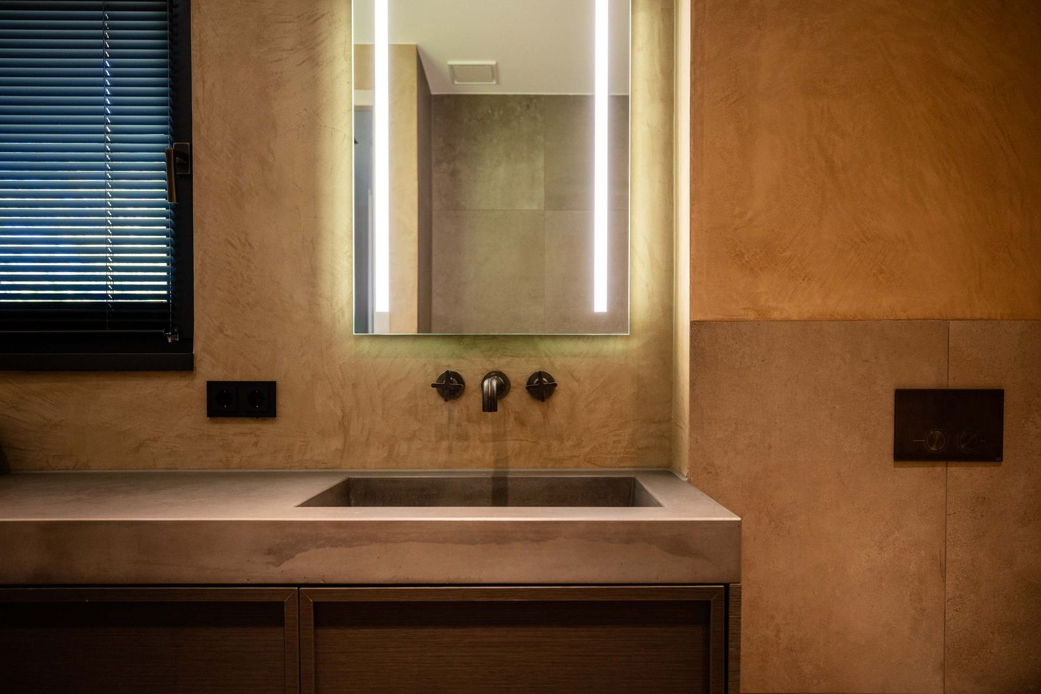 Modern minimalist bathroom vanity with illuminated mirror and concrete sink.