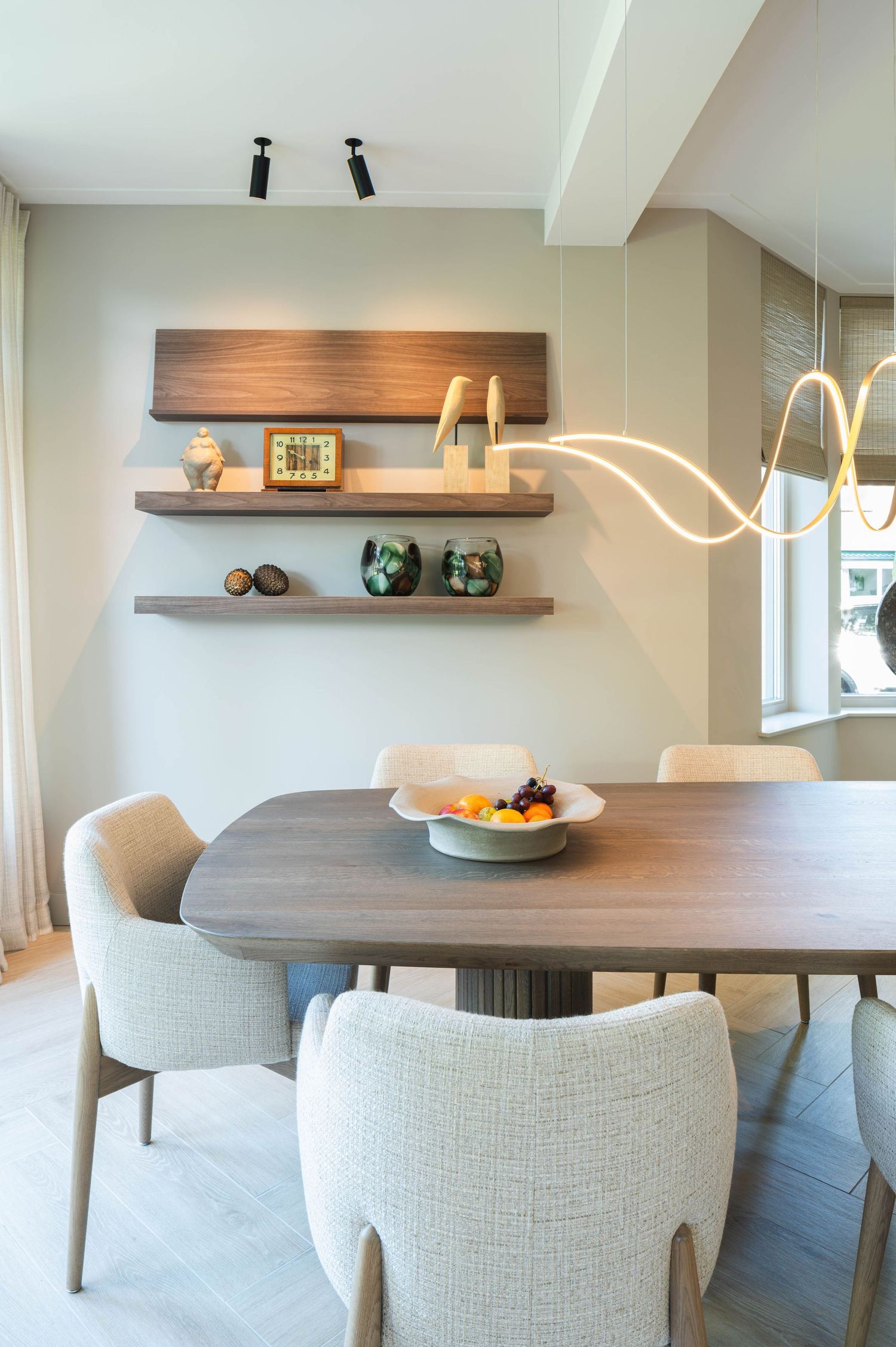 Modern dining room features white upholstered chairs around a wooden table with floating shelves and elegant lighting.