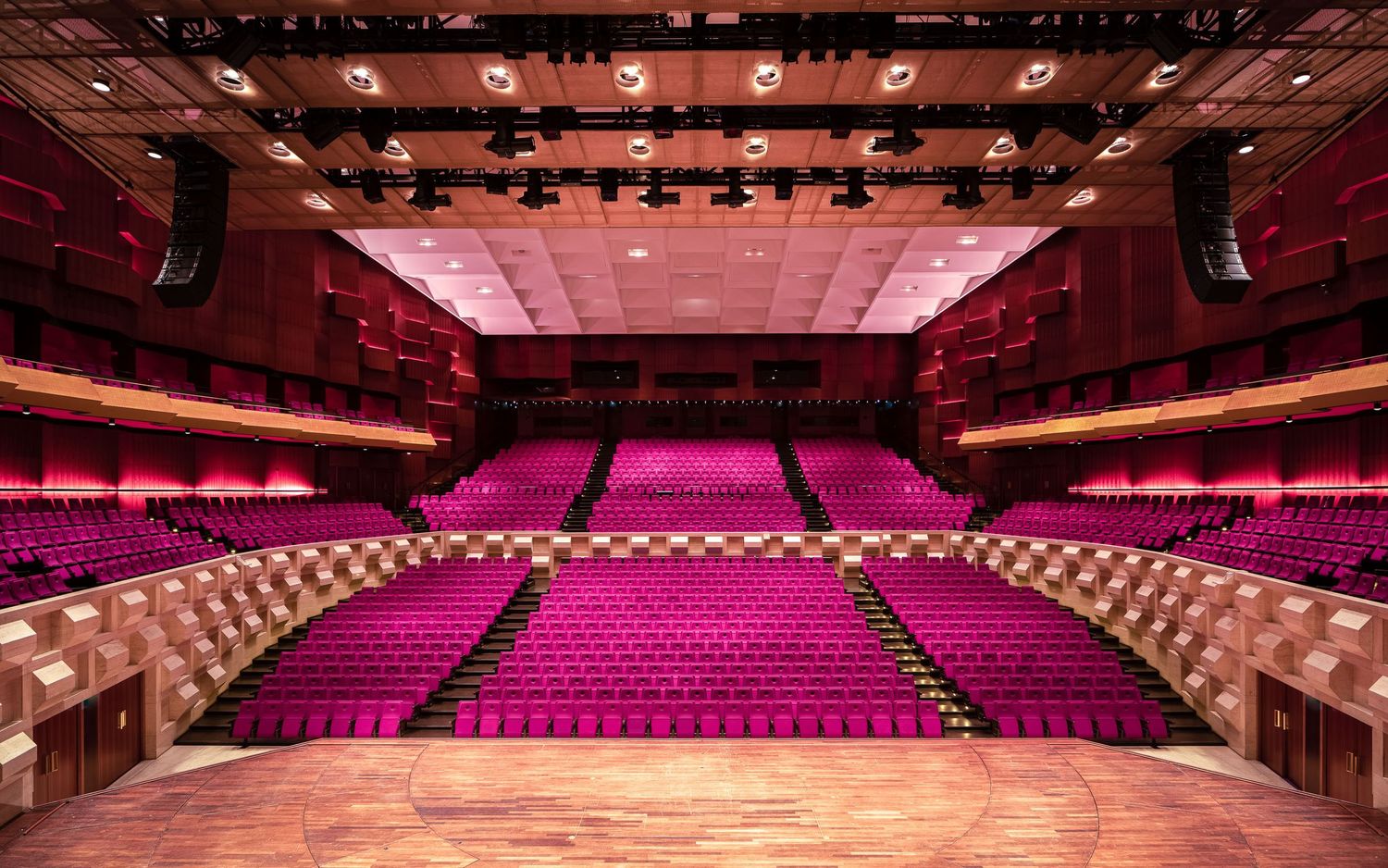 Panoramic view of an empty concert hall with red seats and dramatic lighting illuminating the stage and ceiling.