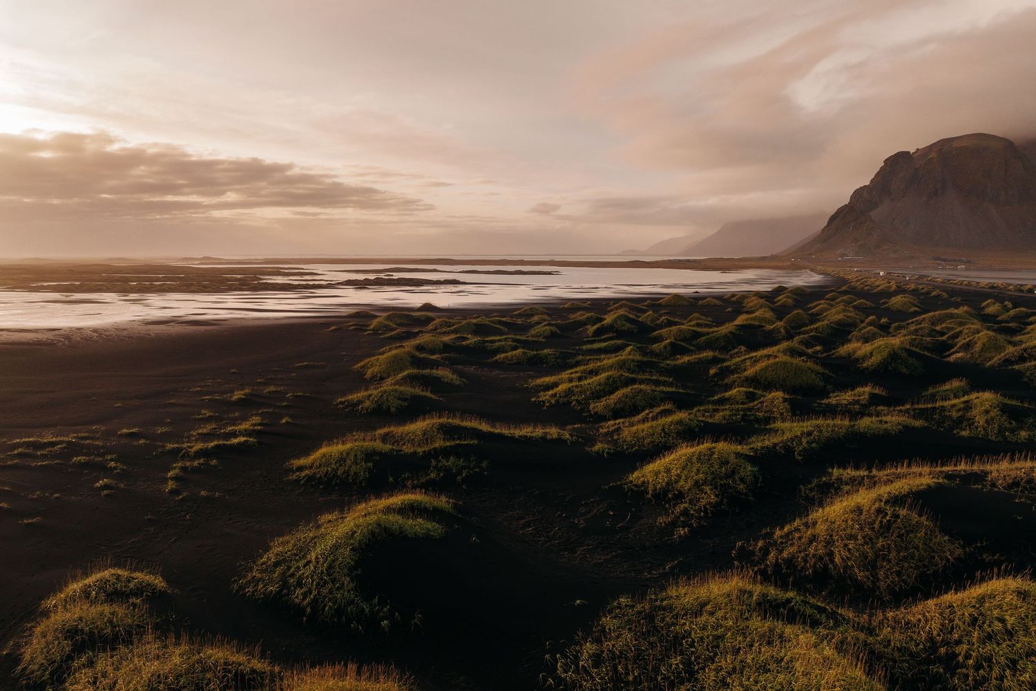 Dramatic sunset over a rugged coastal landscape with mossy green dunes and distant mountains in Iceland.