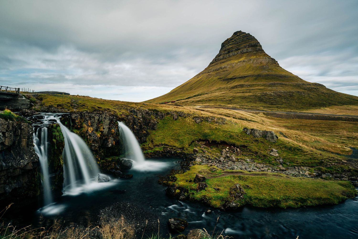Dramatic panoramic view of cascading waterfalls and rugged mountains in the Faroe Islands under moody cloudy skies.