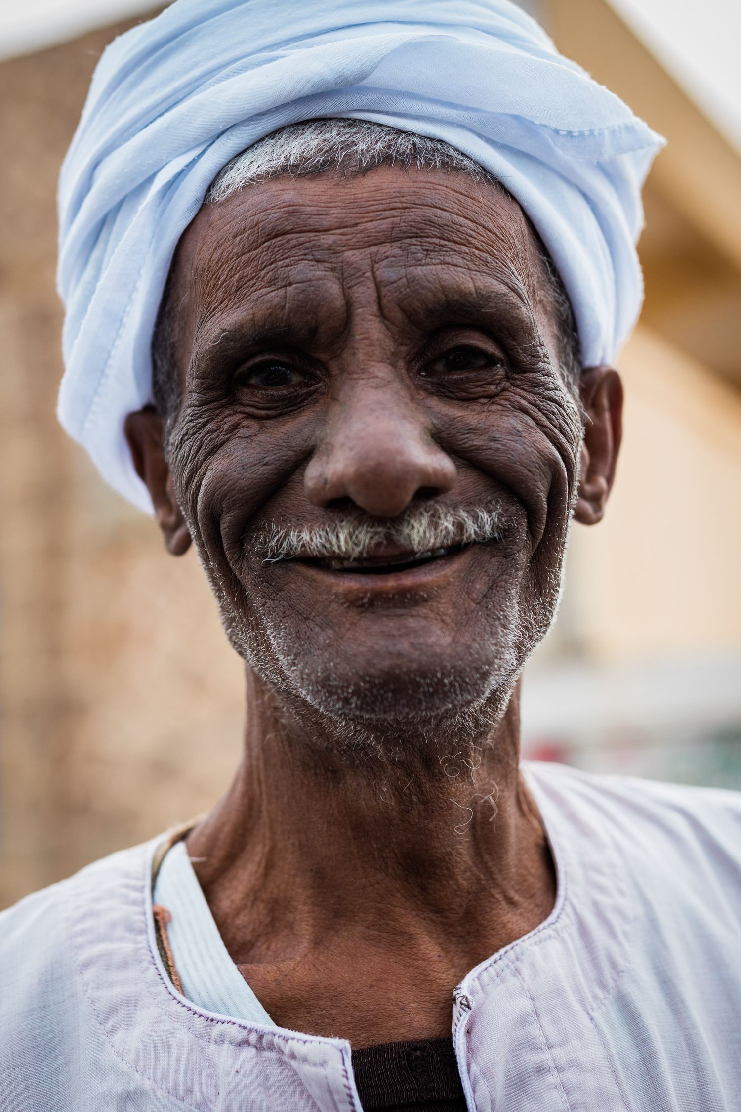 Person wearing traditional white headwrap and garments smiling warmly.