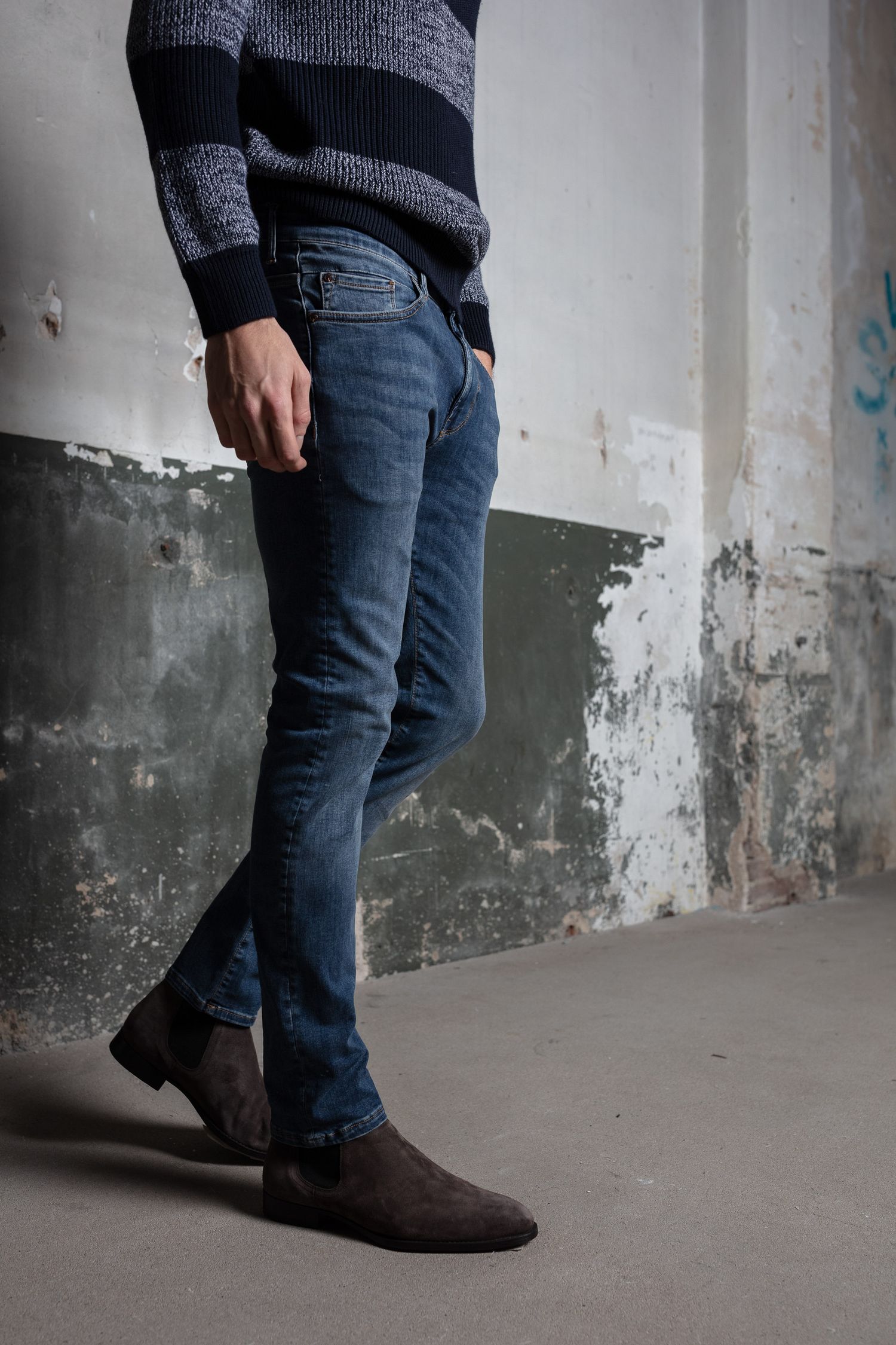 Detail shots of dark denim and boots against industrial concrete wall setting.