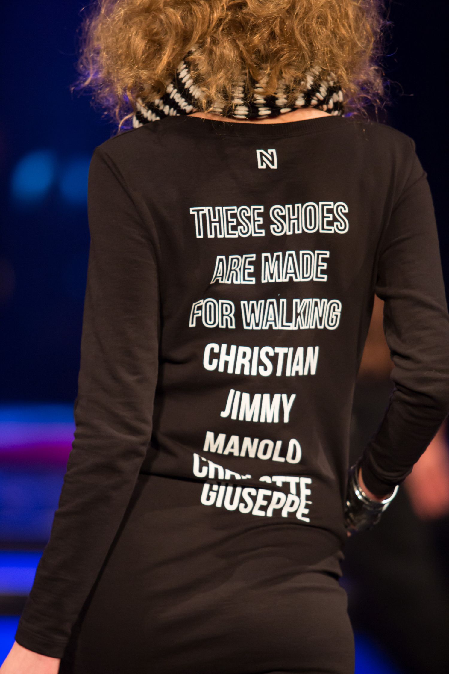 Black long-sleeve shirt with 'These Shoes Are Made For Walking' text listing Christian, Jimmy, Manolo, Charlotte, Giuseppe.